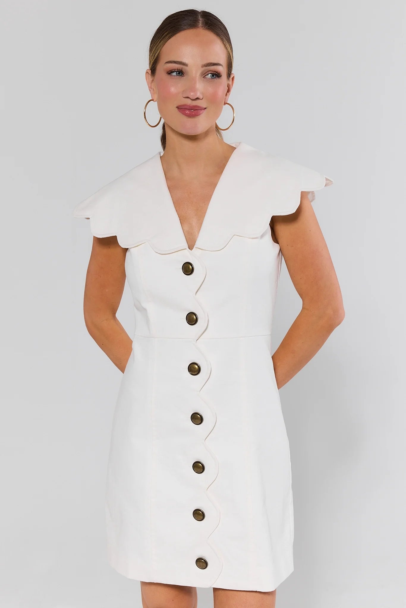 Woman wearing a white dress with buttons on a plain background