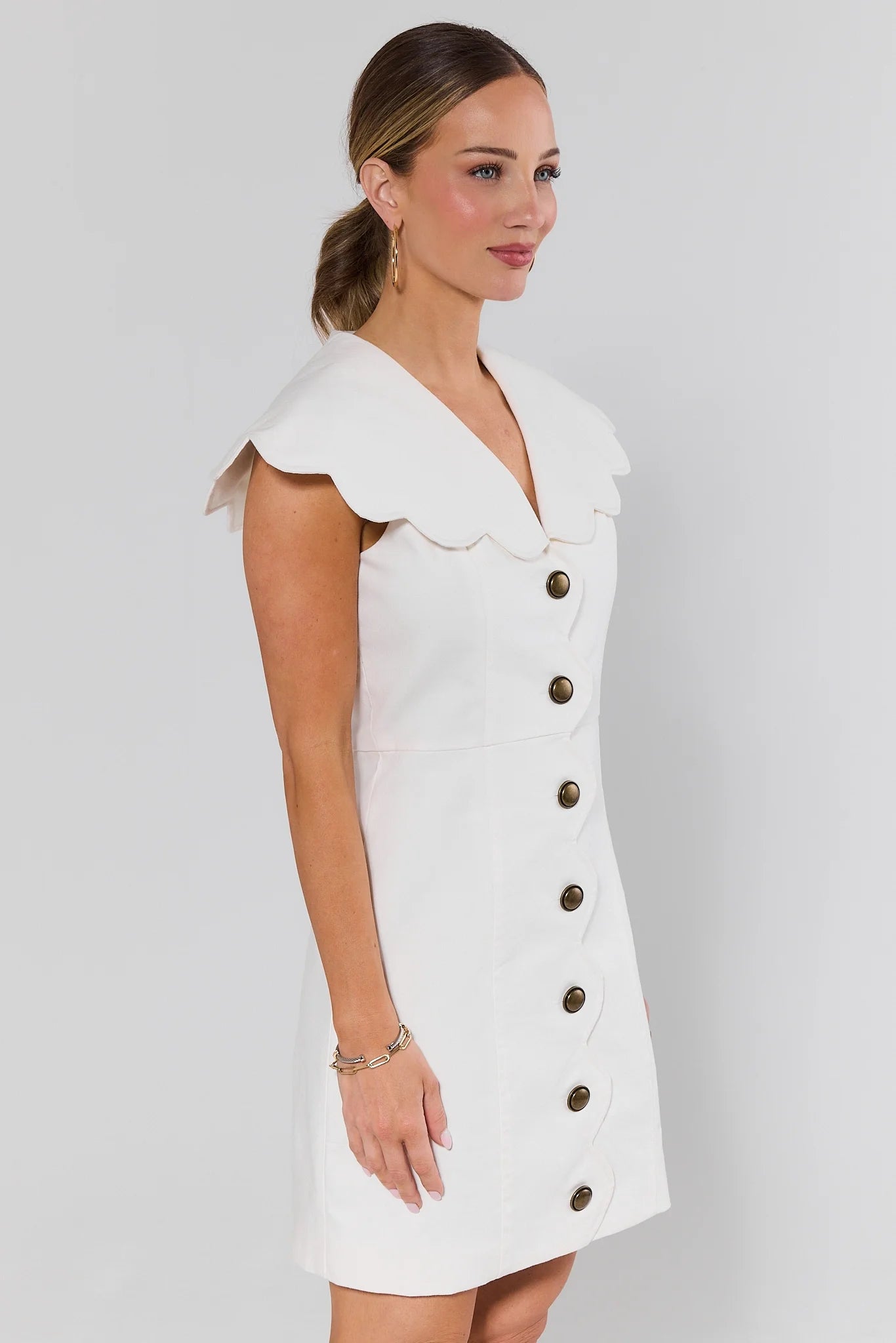 side shot Woman wearing a white dress with buttons on a gray background