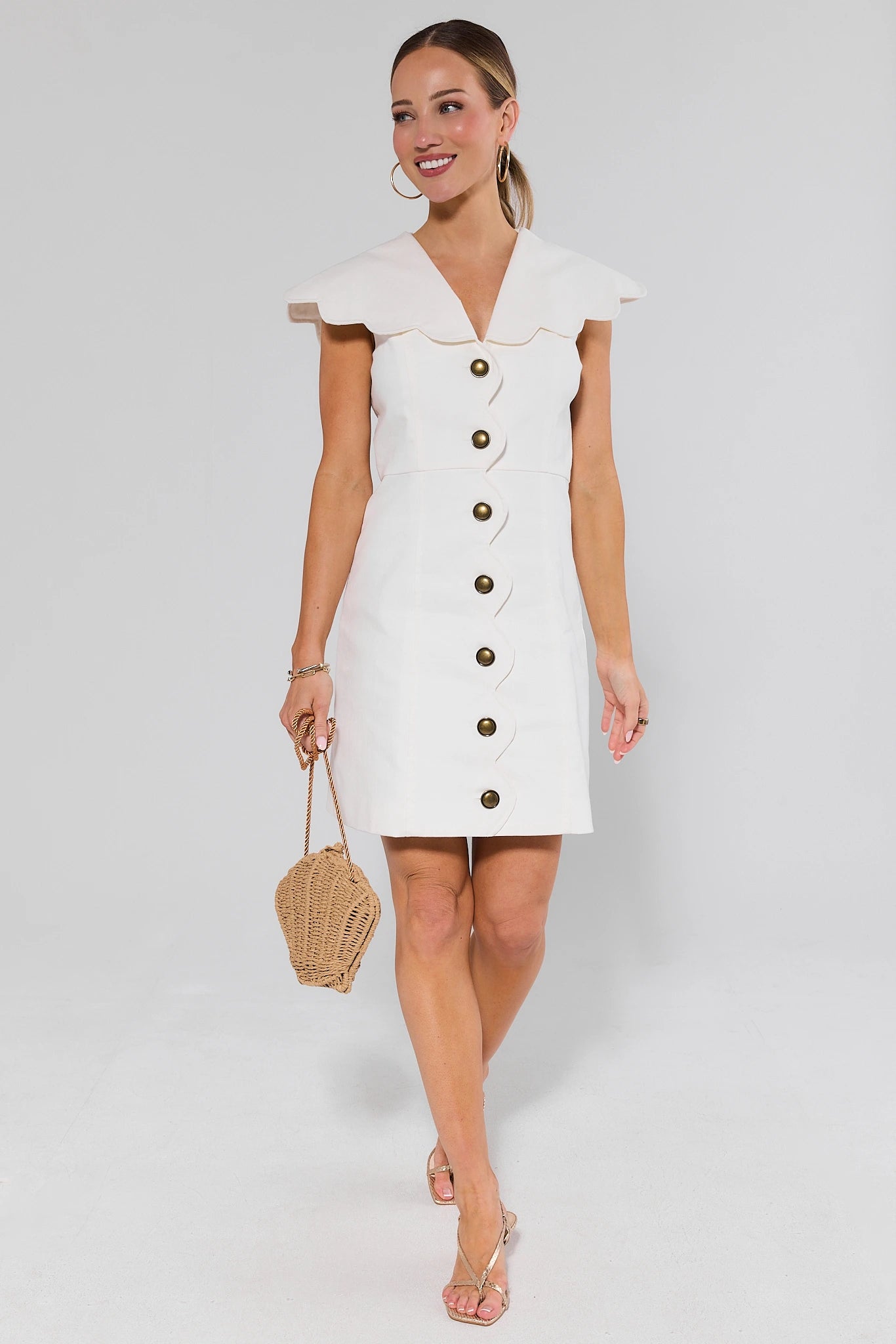 Woman wearing a white dress and gold heels with buttons on a plain background