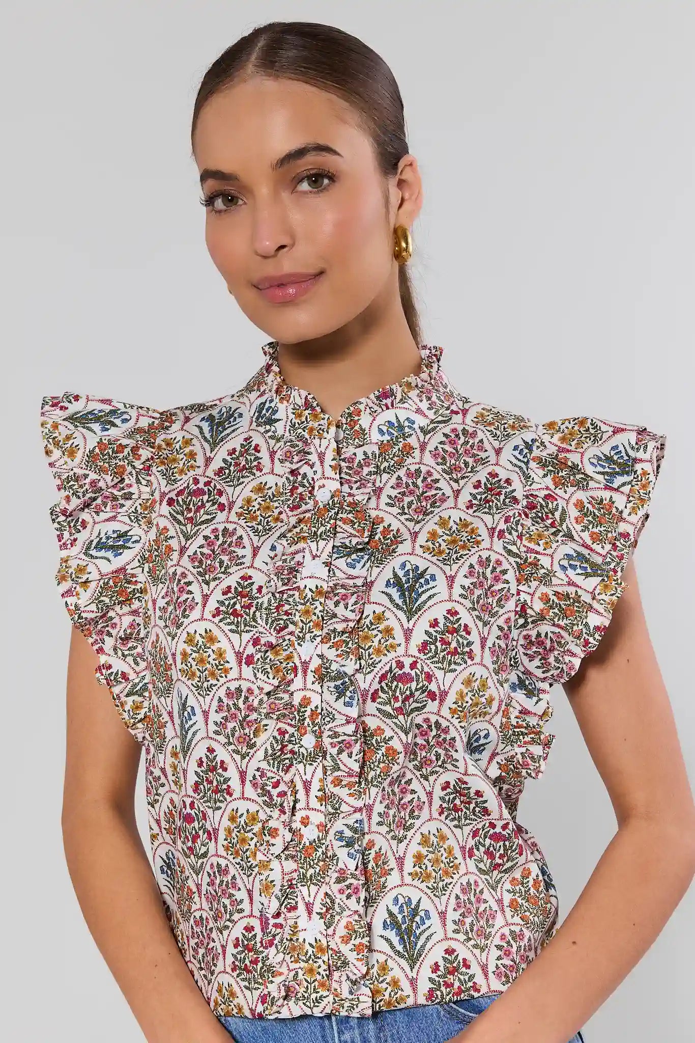 Woman wearing a patterned blouse with ruffled shoulders on a plain background