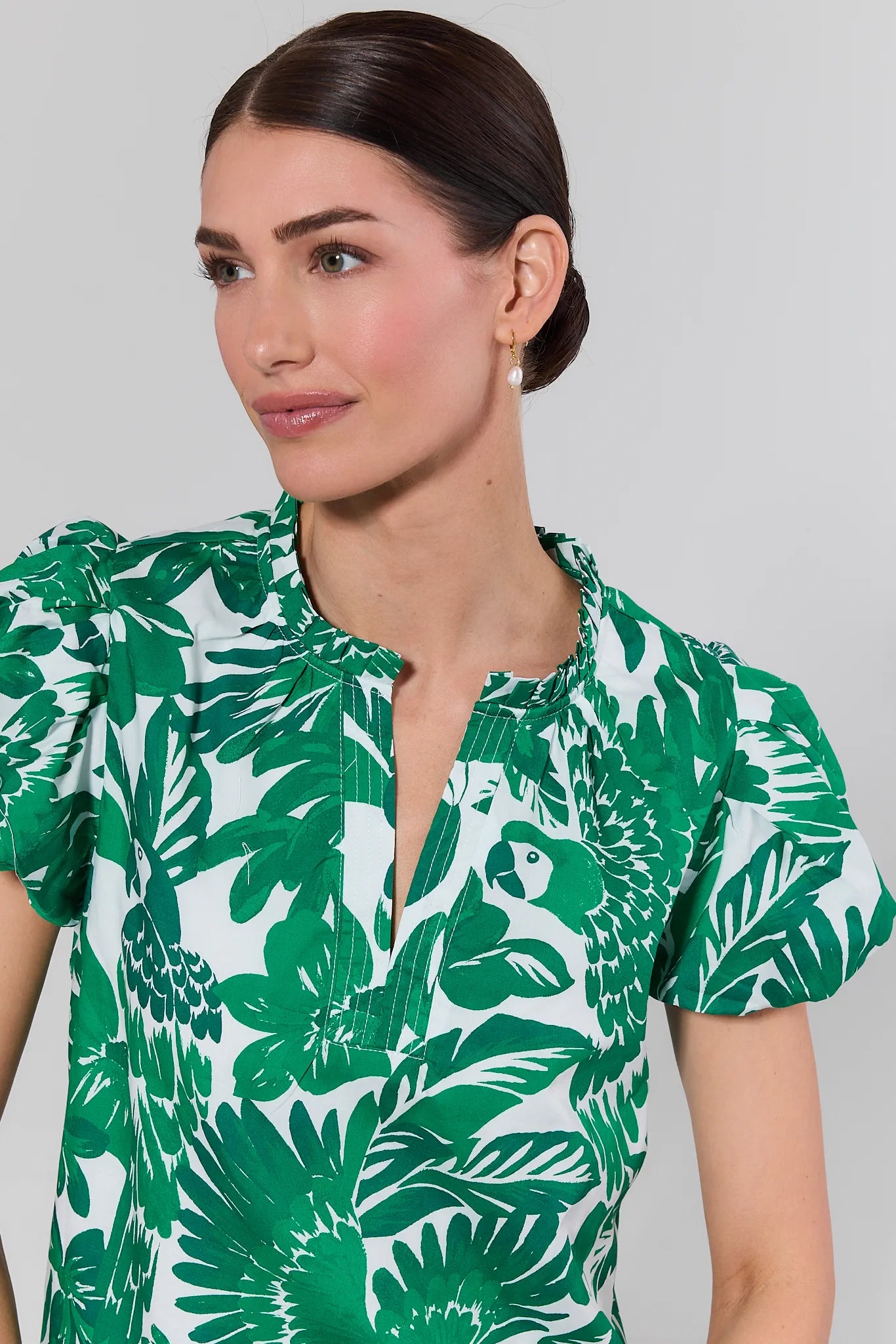 Woman wearing a green and white leaf-patterned shirt against a gray background