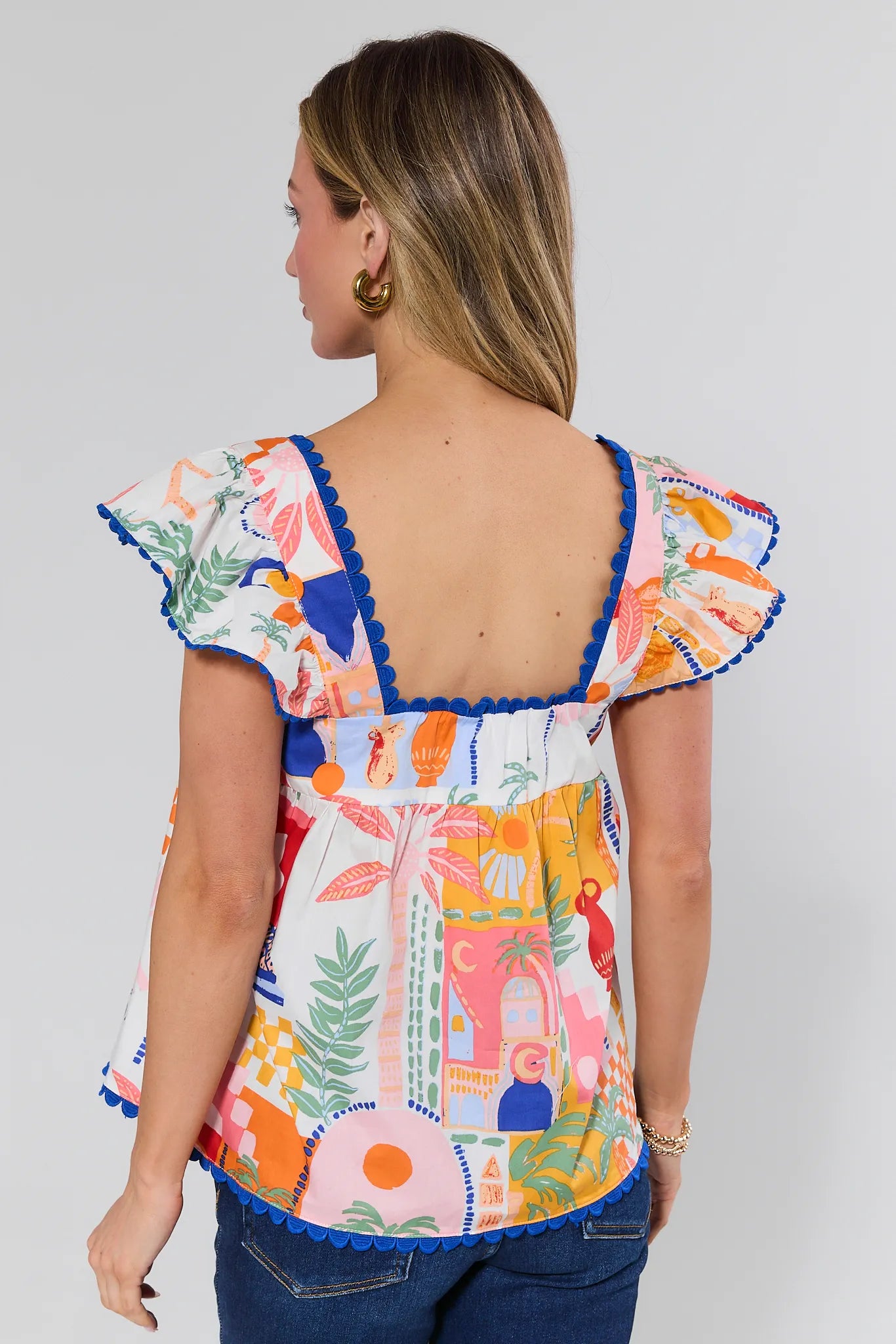 Woman wearing a colorful patterned top with ruffled sleeves on a plain background