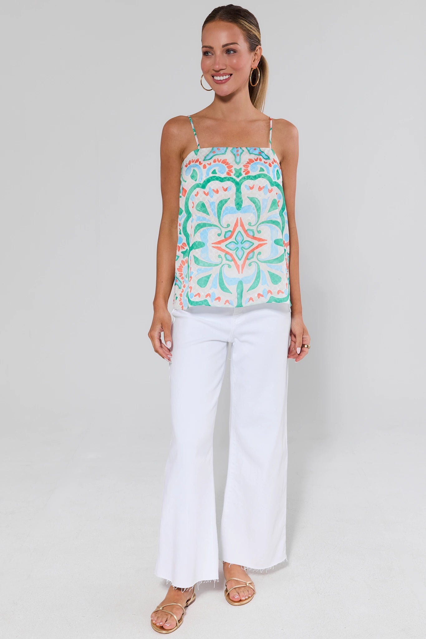 Woman wearing a patterned top and white pants on a plain background