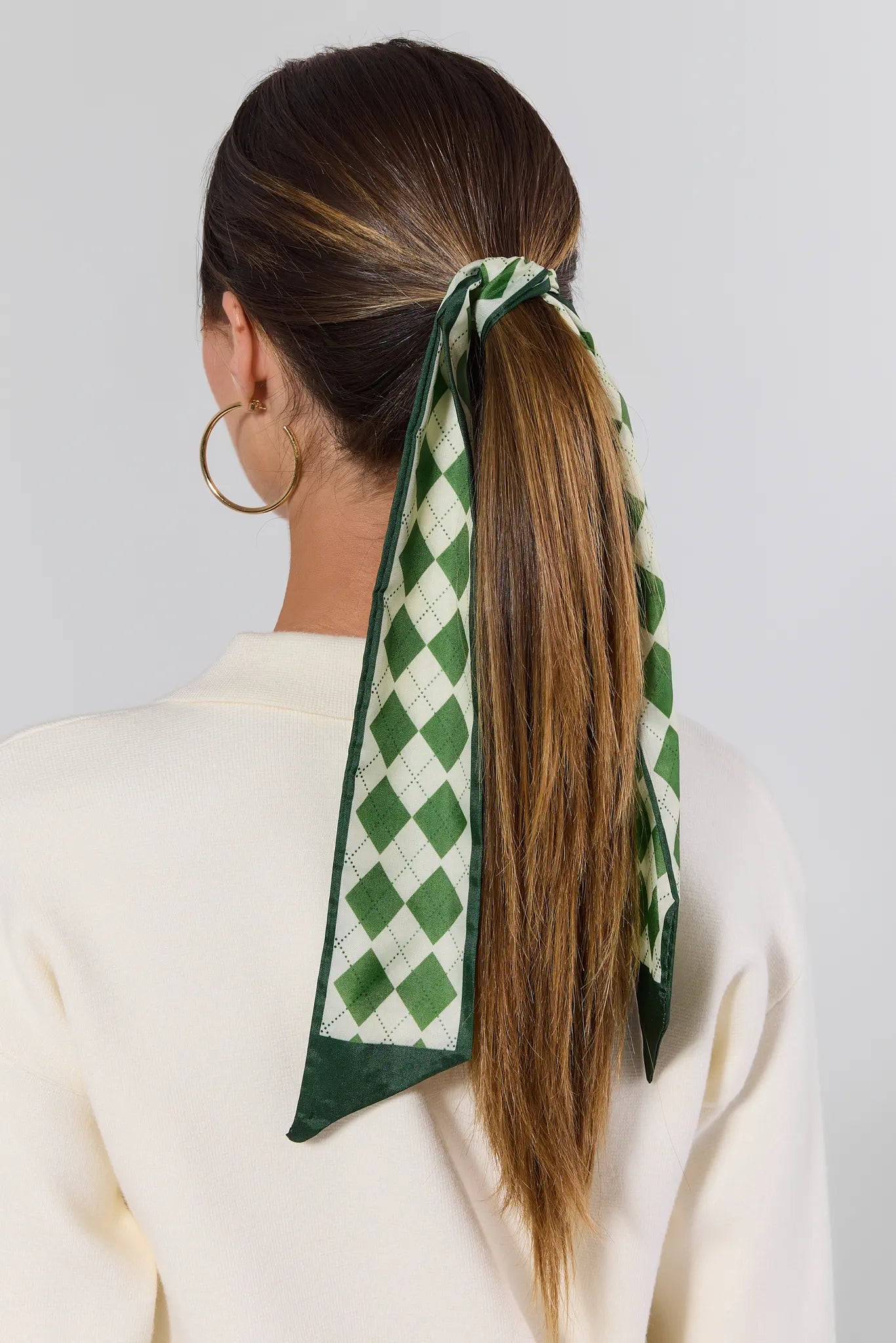 Person with a green and white checkered hair scarf tied around their ponytail on a plain background