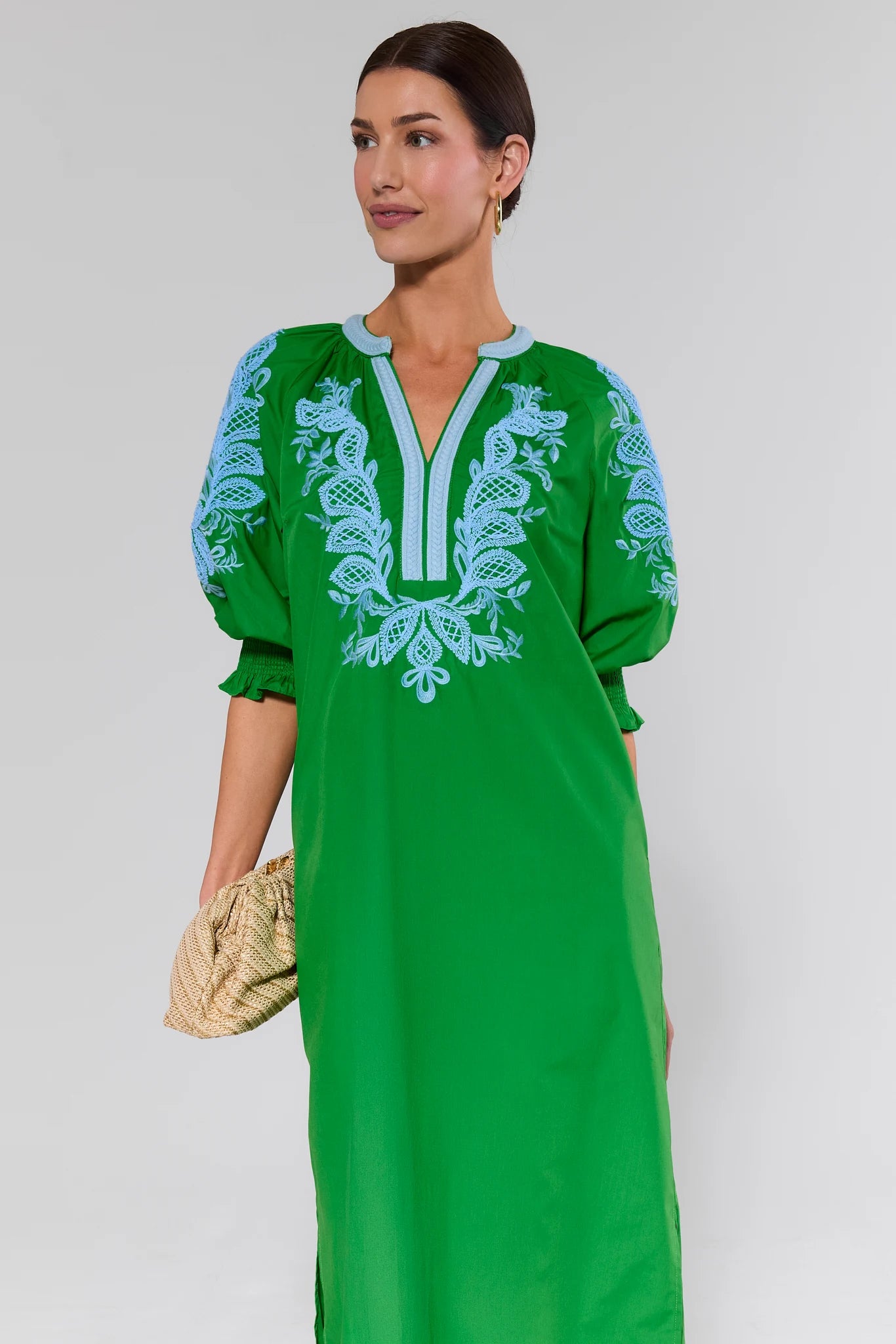 Woman wearing a vivian green dress with white embroidery on a plain background