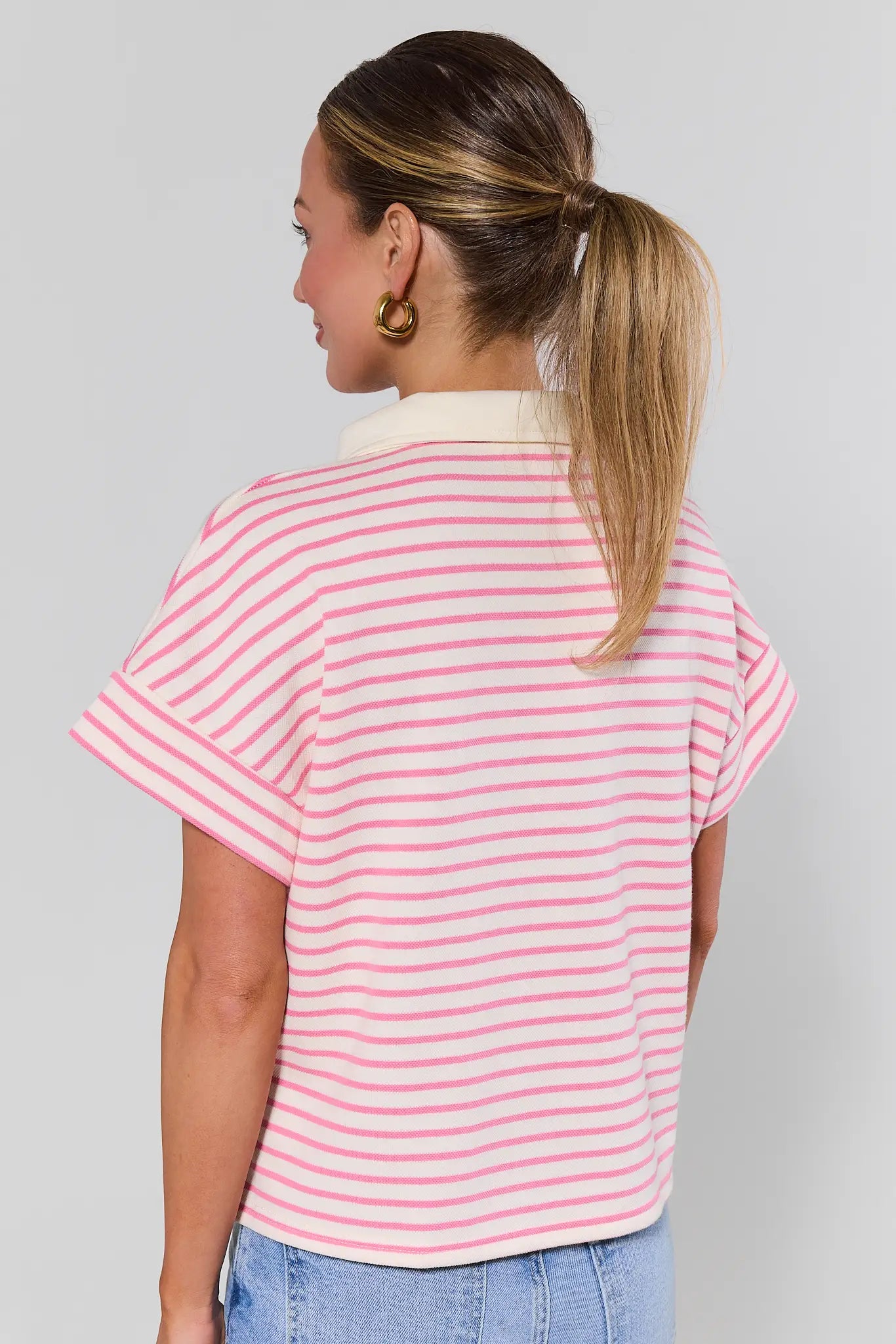 Woman standing wearing a pink and white striped shirt against a gray background