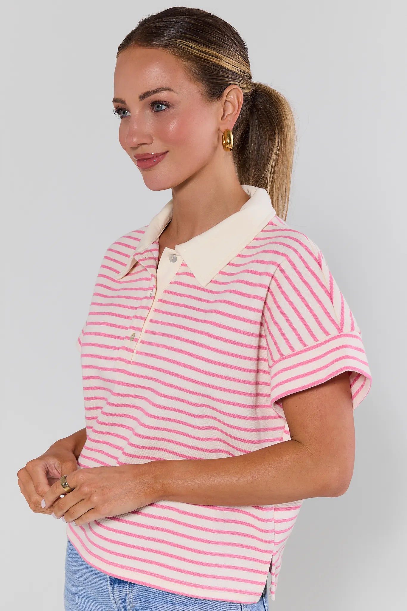 side shot Woman wearing a pink and white striped polo shirt against a gray background