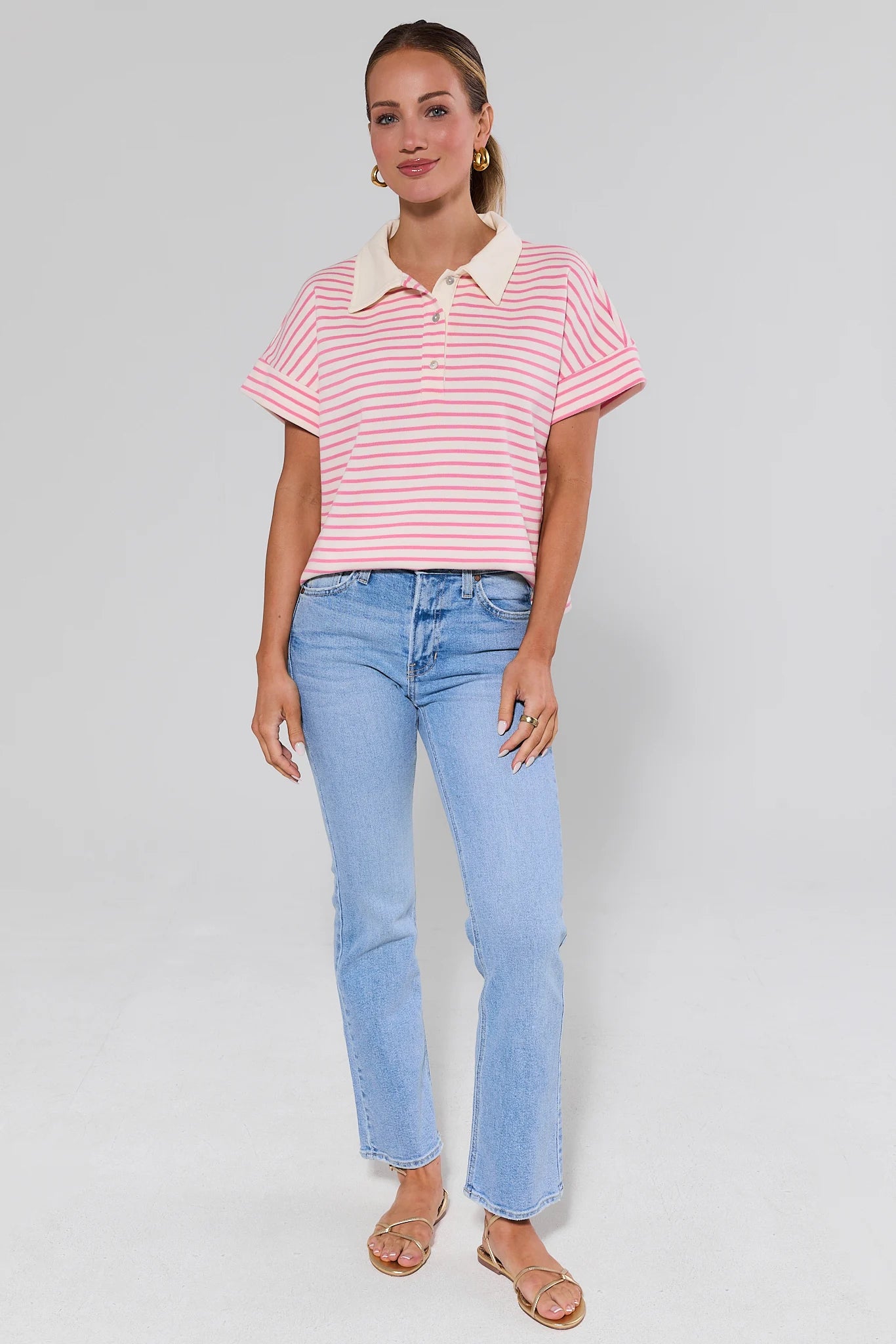 Woman wearing a pink and white striped shirt with a collar and light blue jeans on a gray background