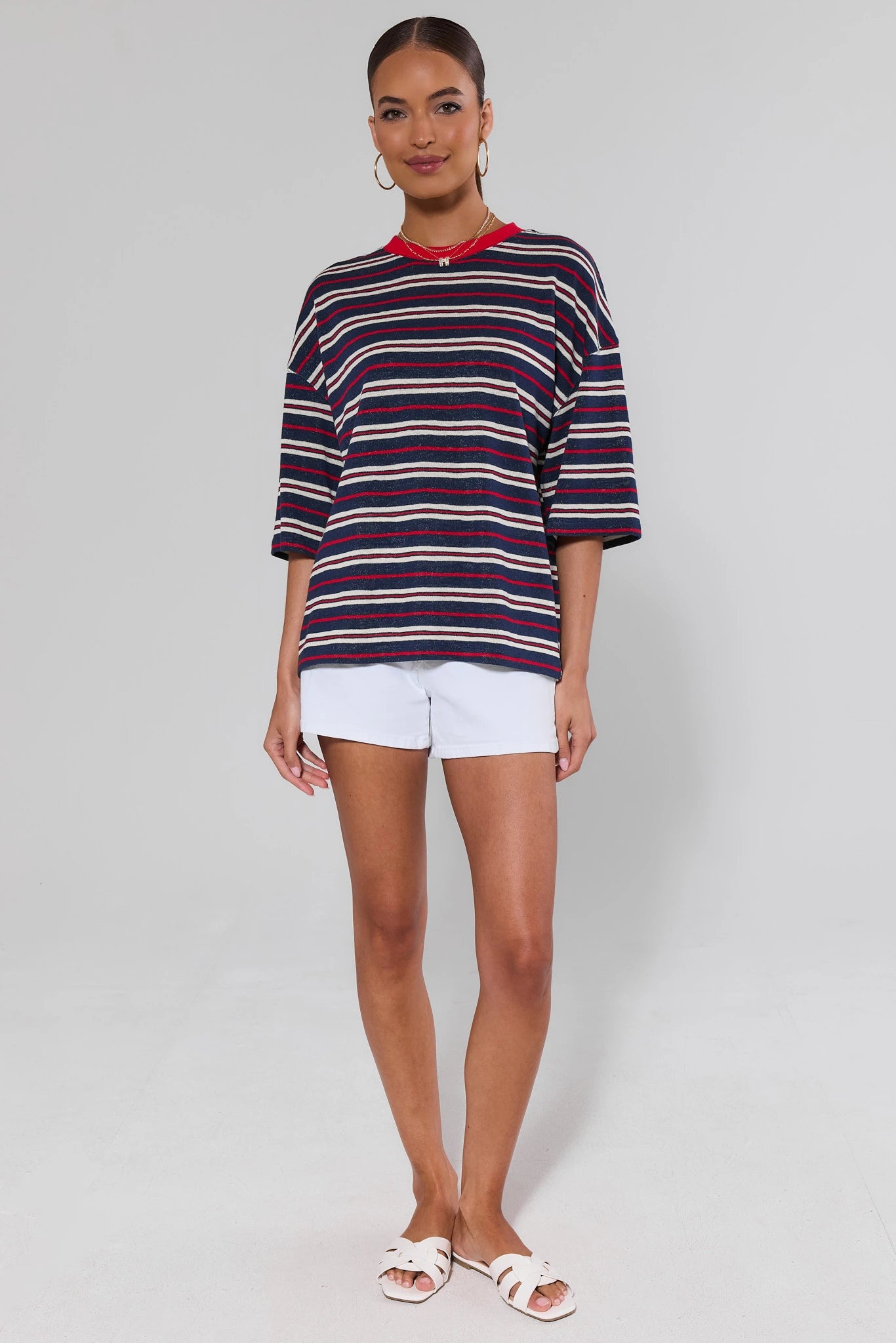 Woman wearing a mary striped sweater and white shorts on a plain background