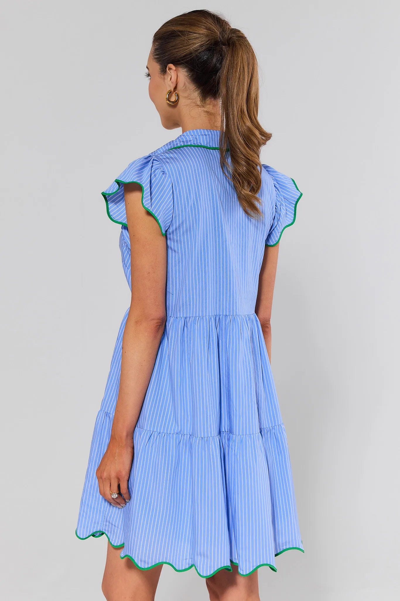 Woman standing wearing a blue dress with green trim on a gray background