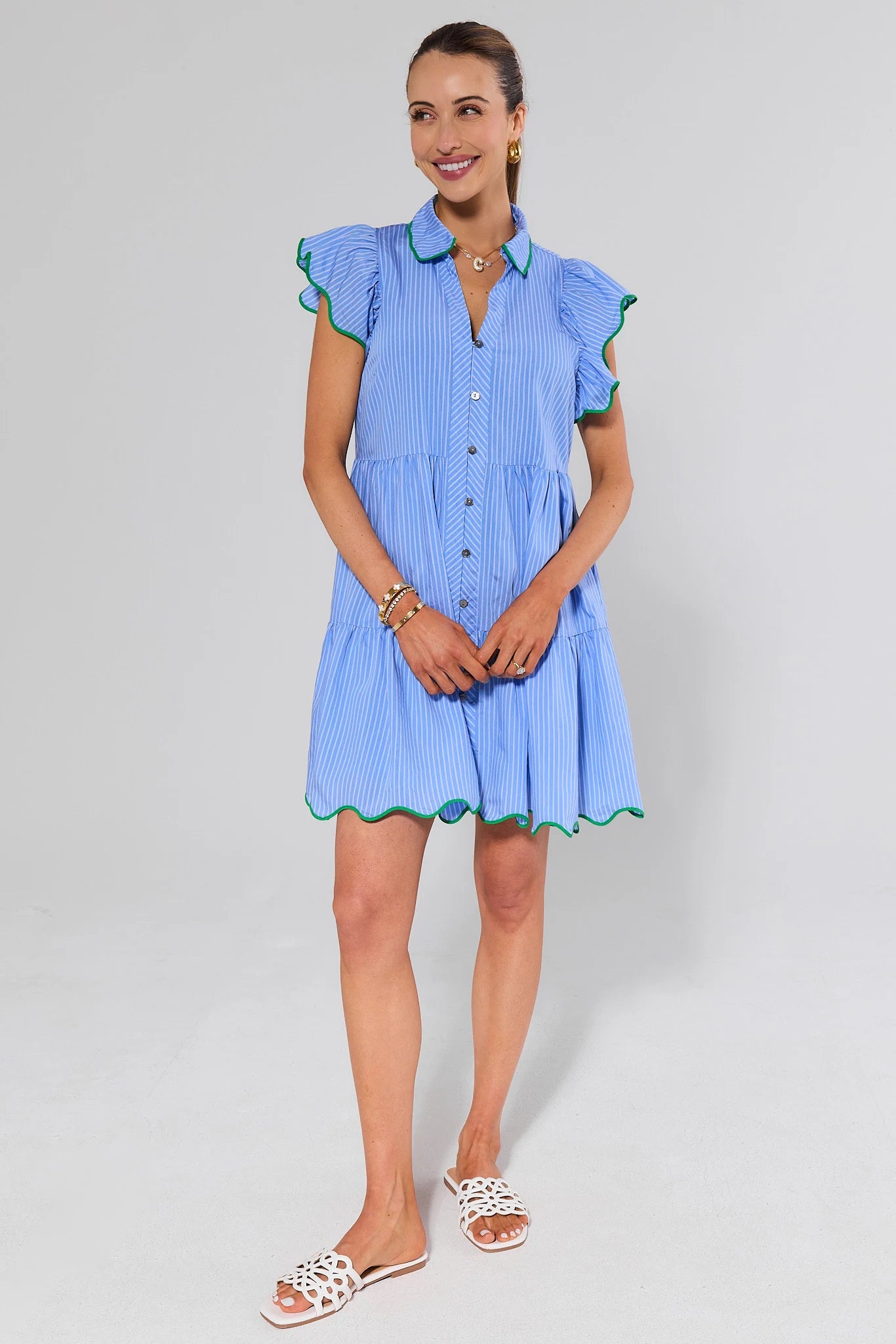 Woman wearing a blue dress with green trim and white sandals on a white background