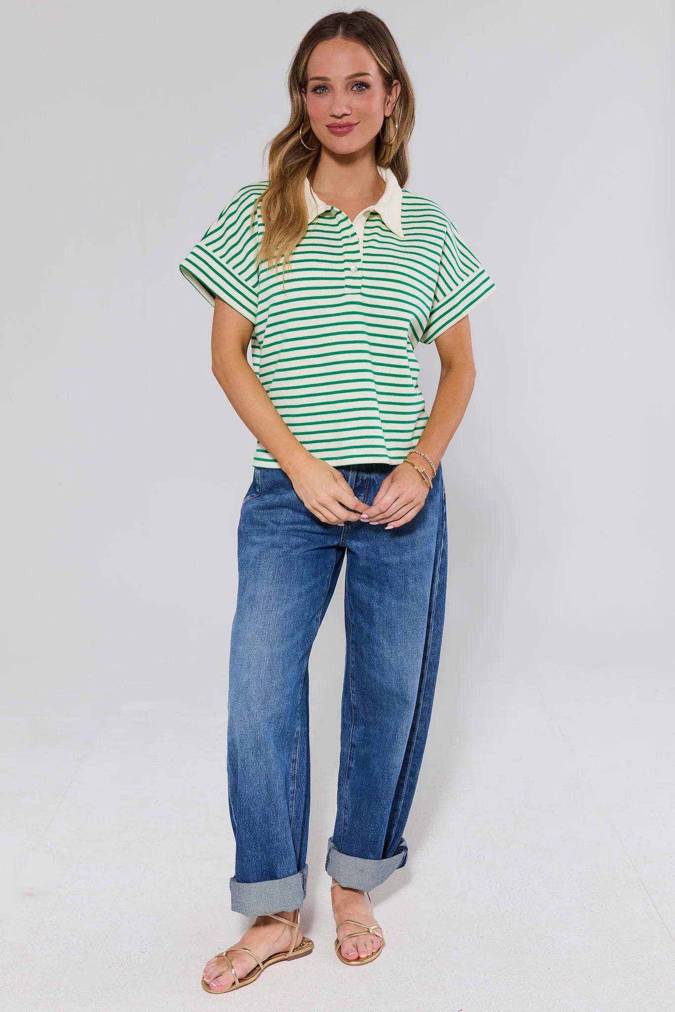 Woman wearing a green and white striped polo shirt and blue jeans on a plain background