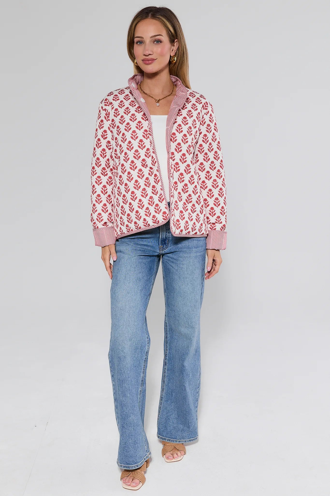 Woman wearing a red floral patterned jacket and blue jeans on a white background