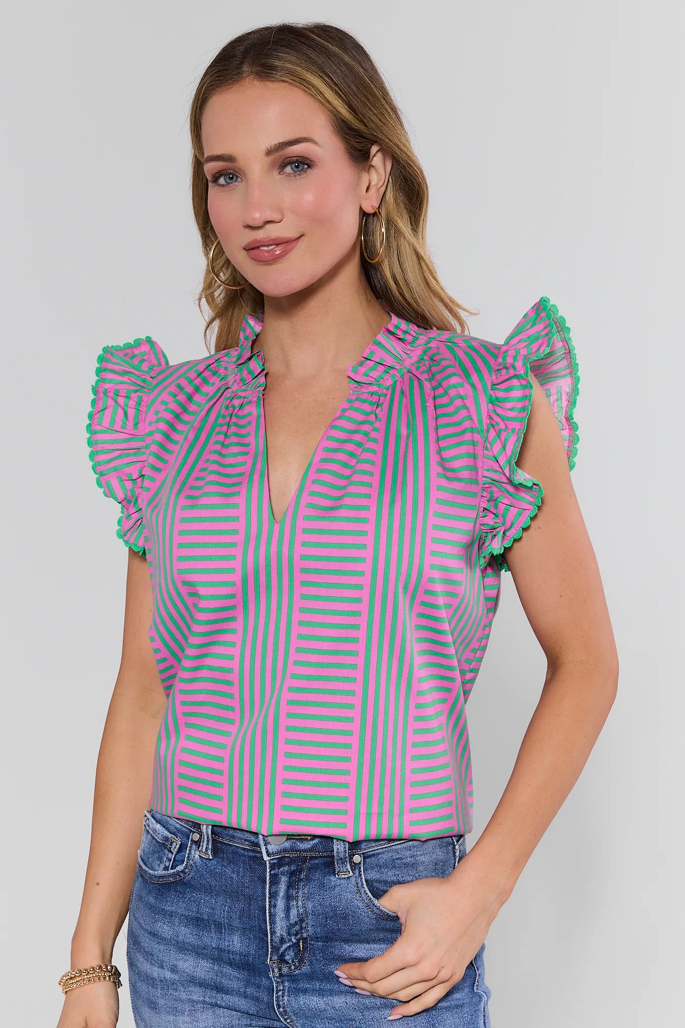 Woman wearing a pink and green striped blouse with ruffled sleeves on a white background