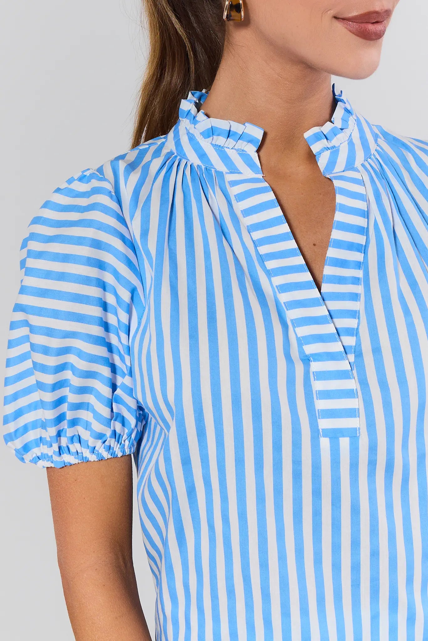 Close-up of a person wearing a blue and white striped shirt against a gray background