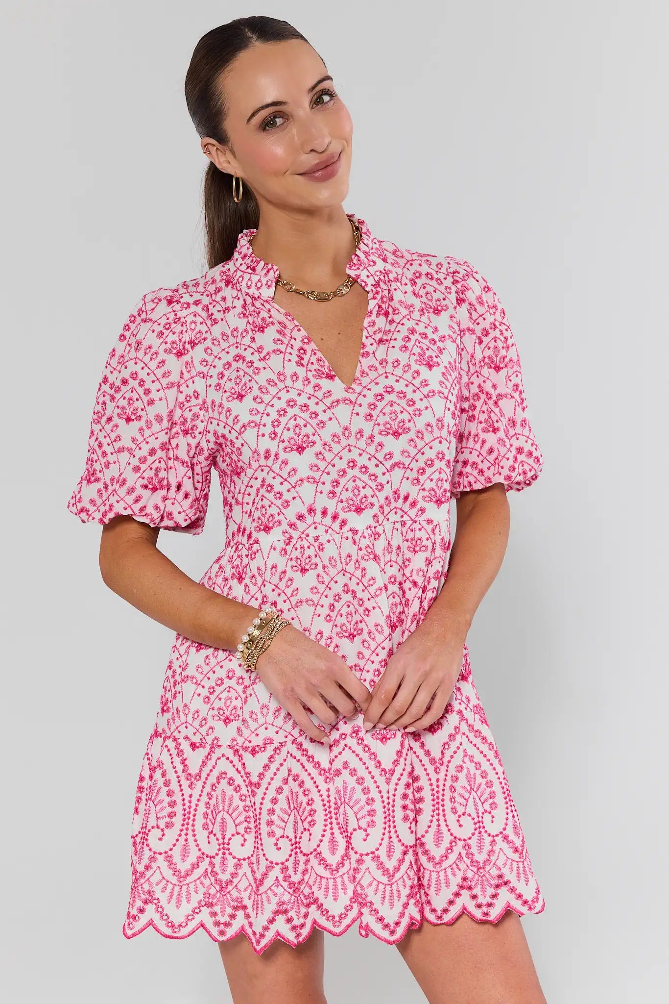 Woman wearing a pink and white floral dress with lace hem on a plain background