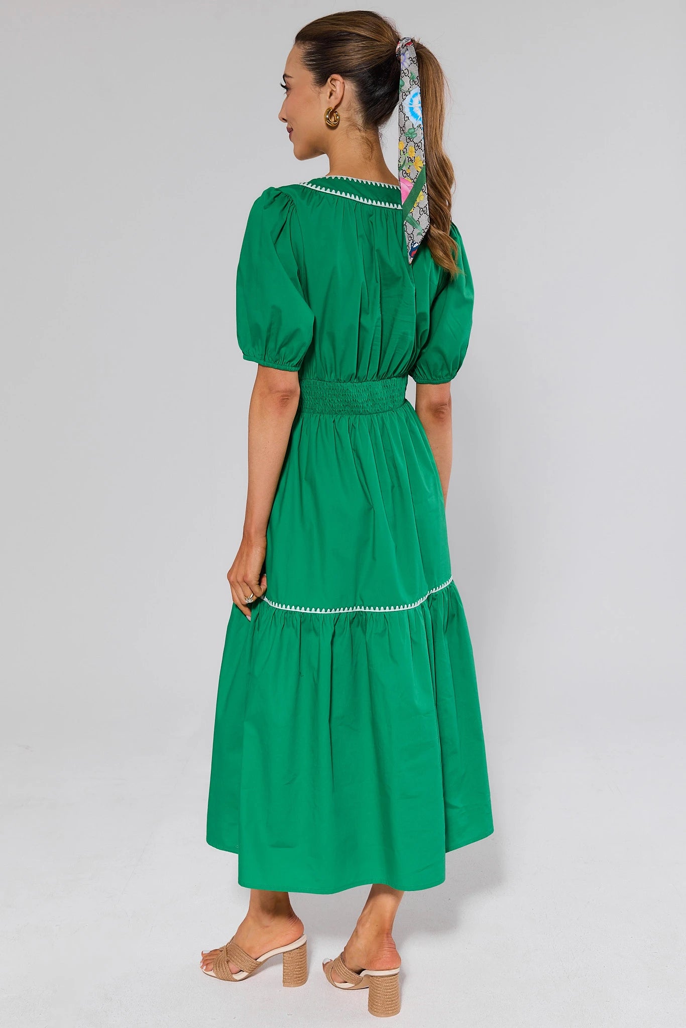 Woman standing wearing a green dress with a white trim on a plain background