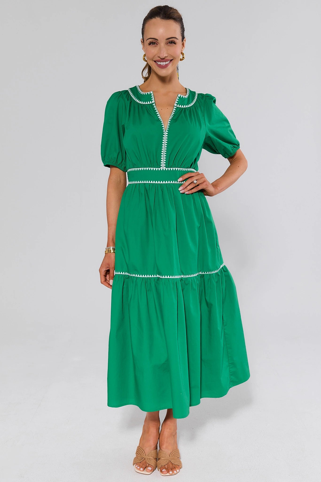 Woman wearing a green dress with white embroidery and heels on a gray background