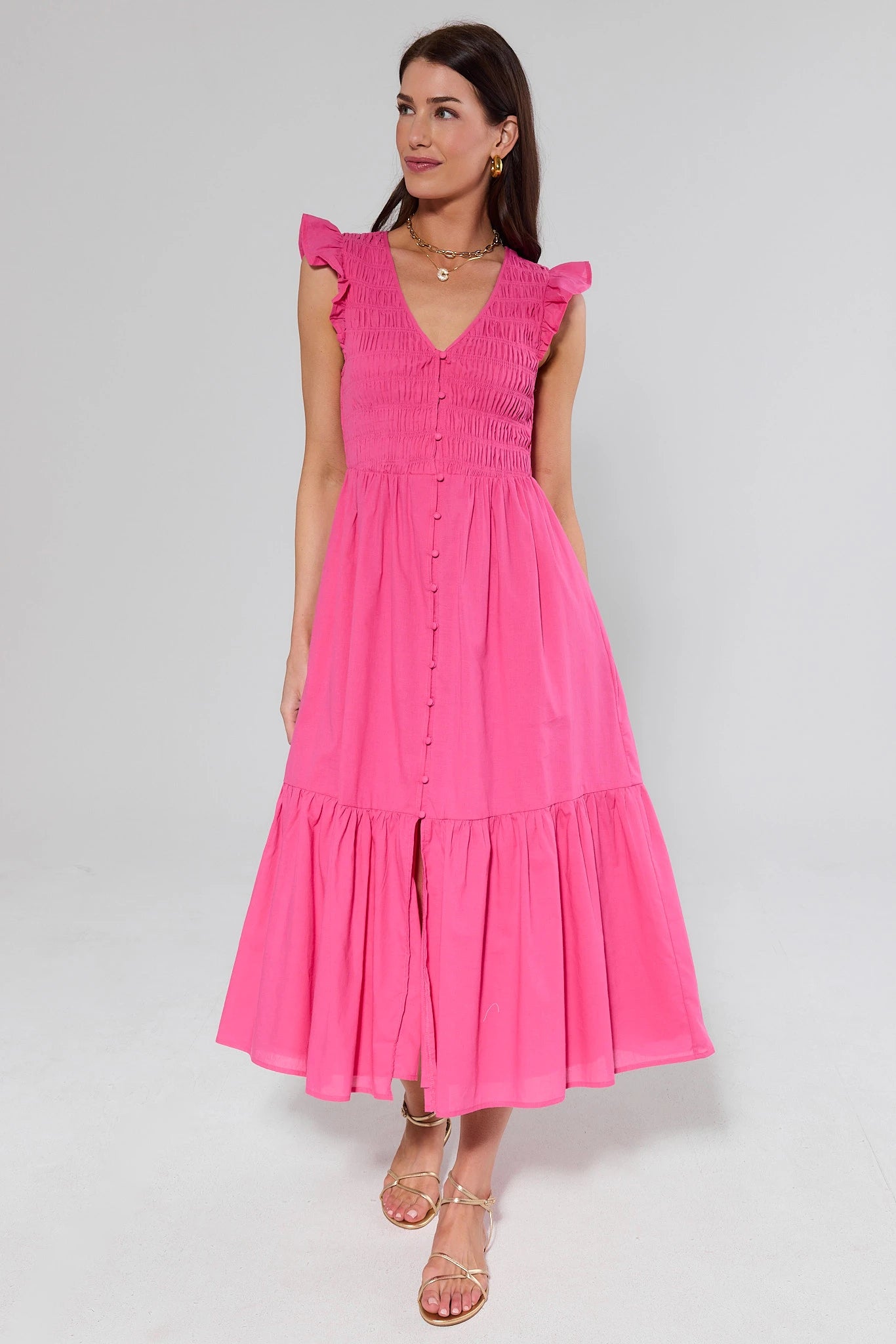 Woman wearing a pink dress with ruffled sleeves and flats on a white background