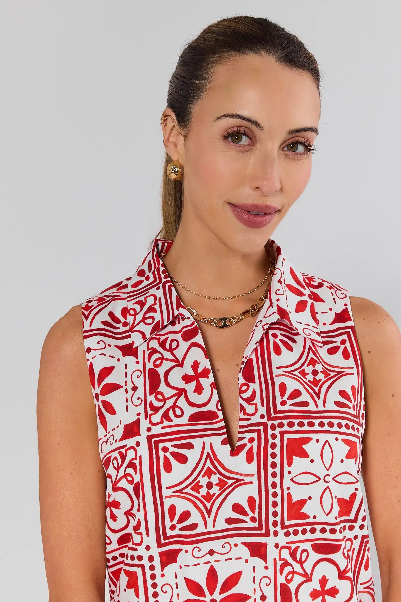 close up Woman wearing a red and white patterned sleeveless top against a plain background