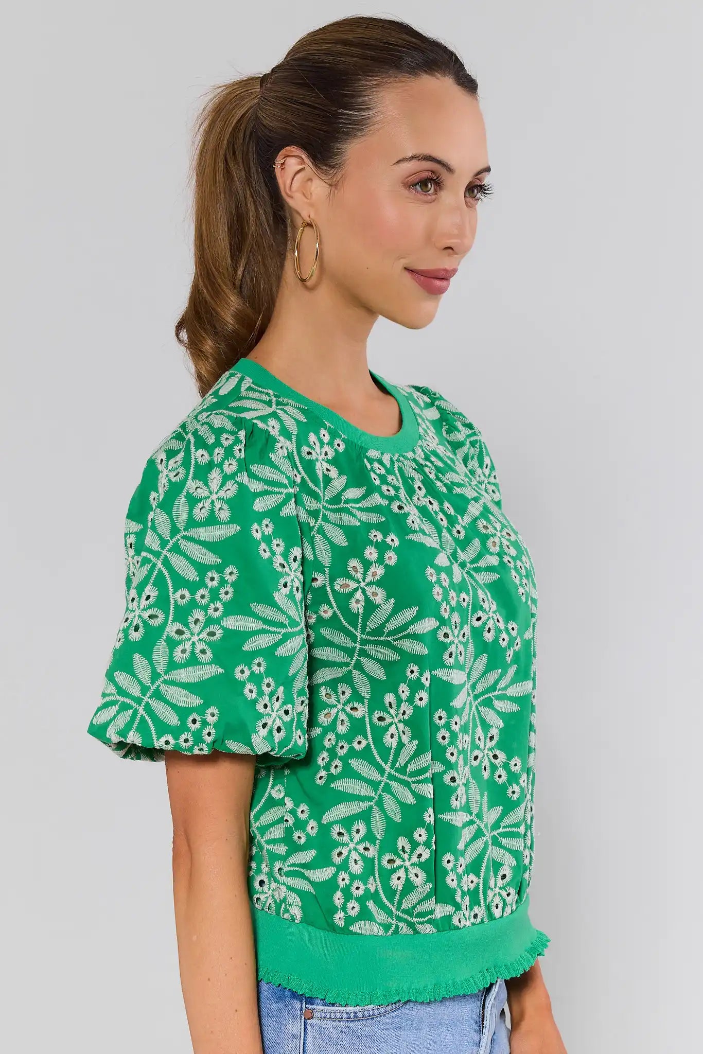 side shot Woman wearing a green floral blouse against a gray background