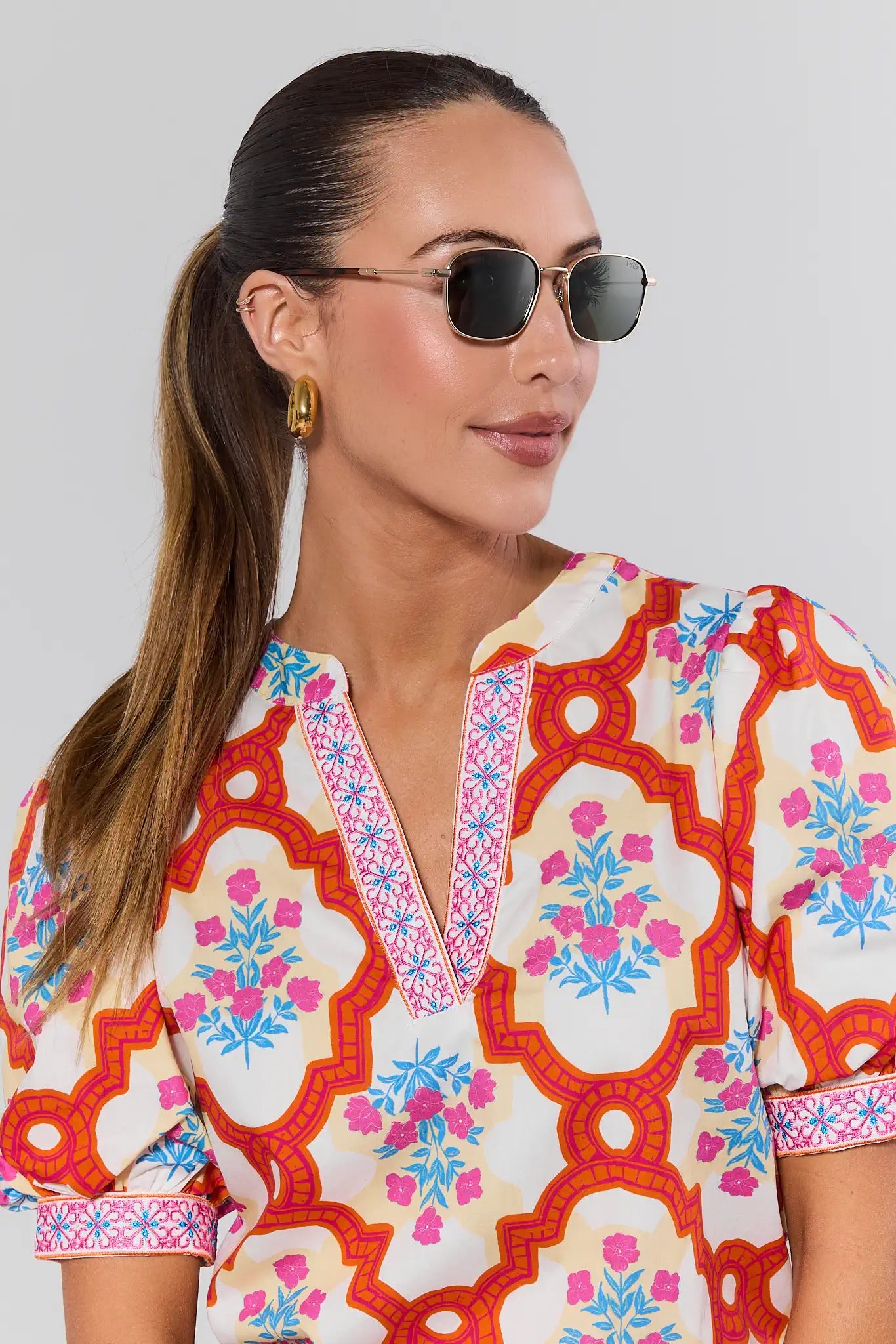 Woman wearing a colorful patterned shirt with sunglasses against a plain background