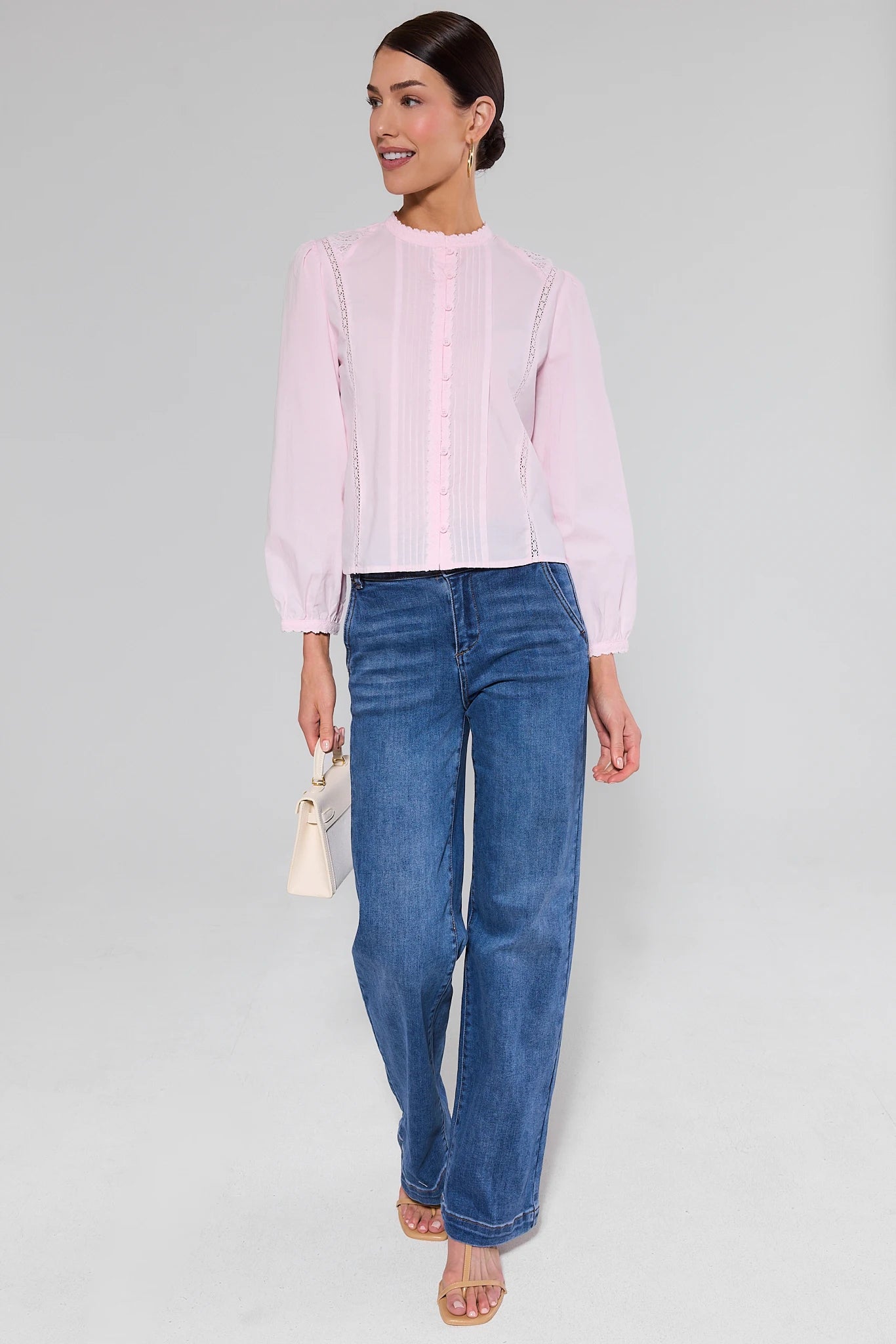 Woman wearing a light pink blouse and blue jeans on a plain background