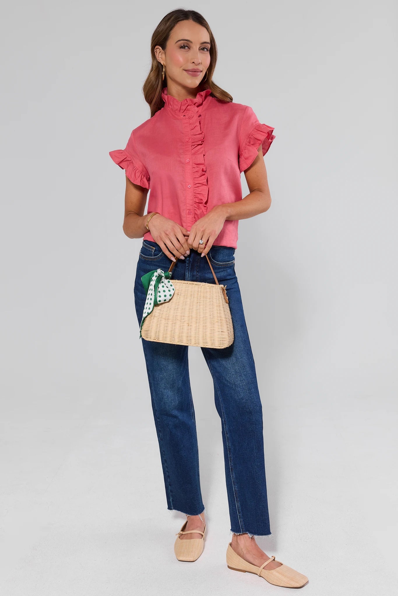 Woman wearing a pink blouse and blue jeans, holding a beige handbag with a green leaf design.