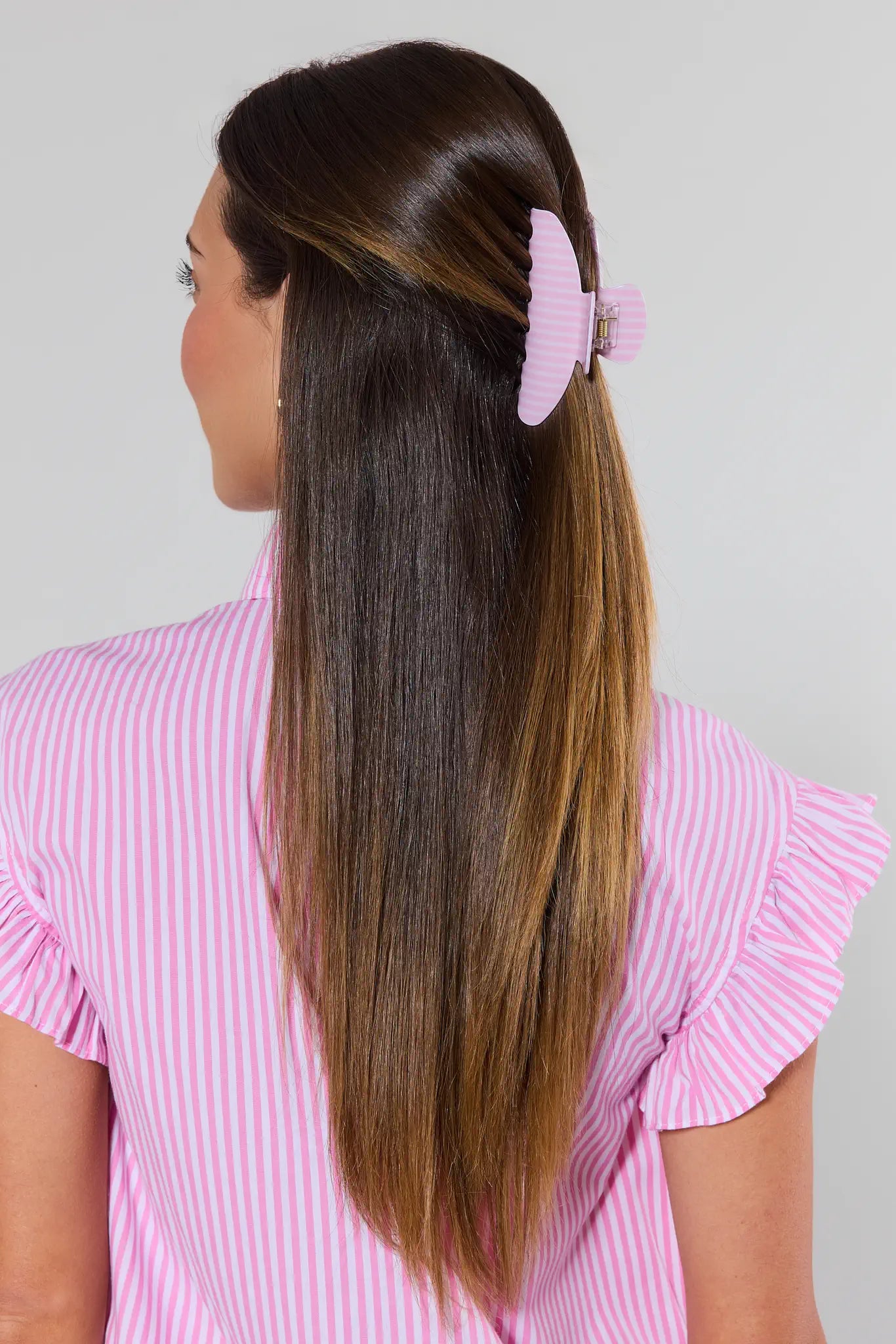 Person with long hair wearing a pink hair clip against a gray background