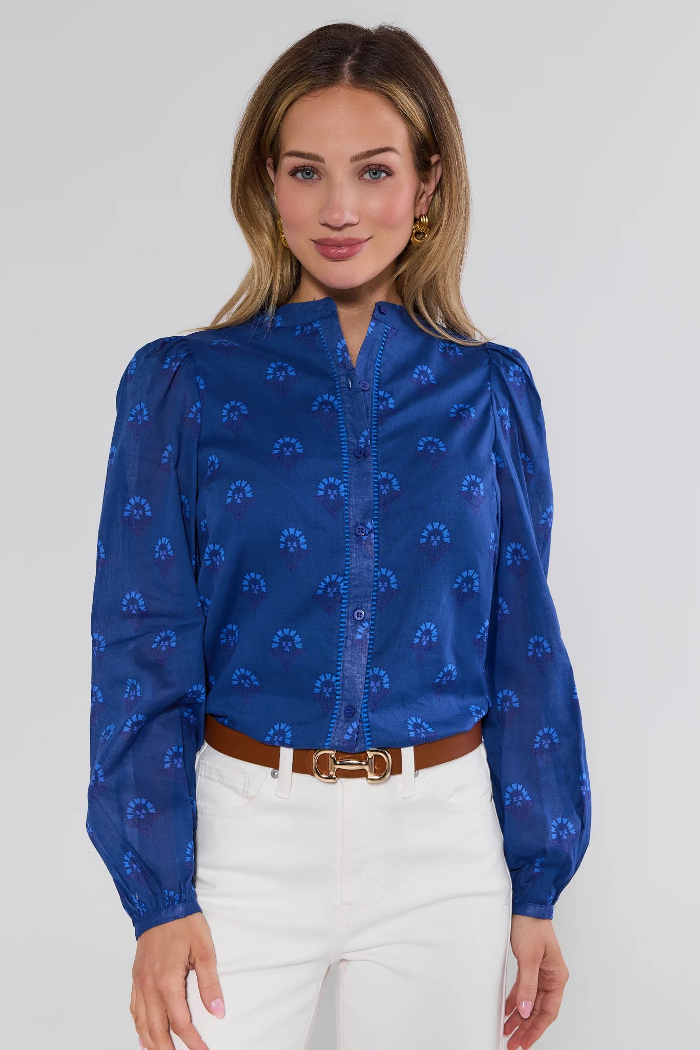 Woman wearing a blue patterned blouse with white pants on a plain background