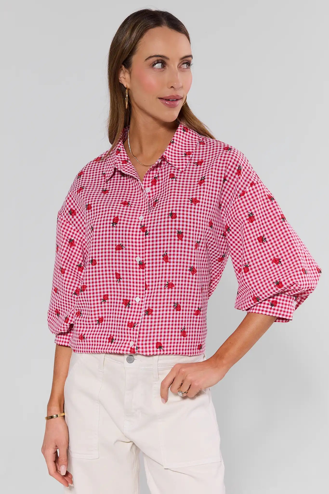 Woman wearing a red and white checkered blouse with rolled-up sleeves on a plain background