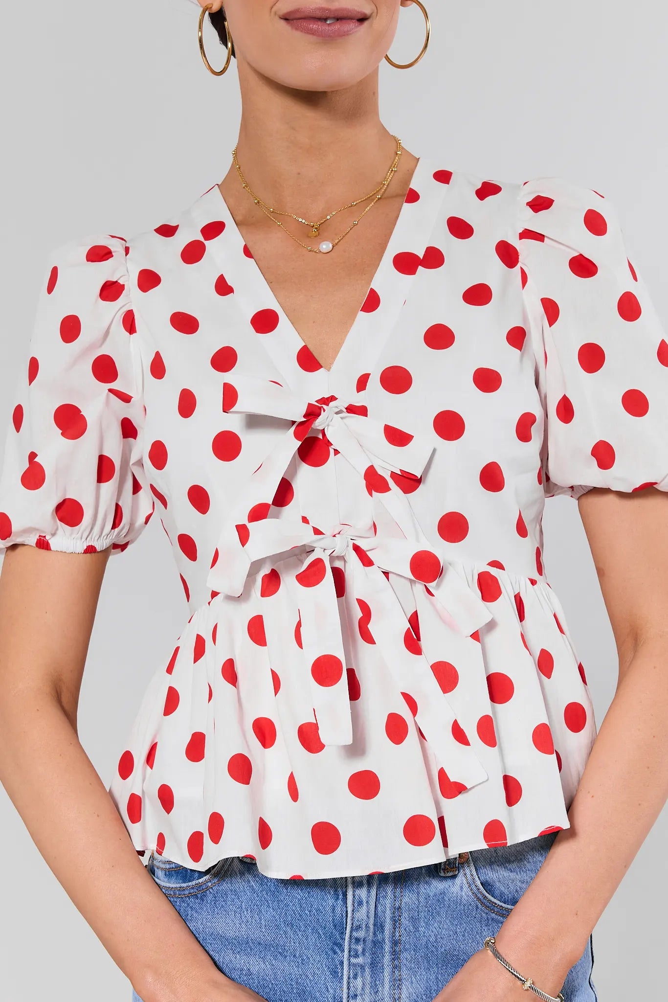 close up Woman wearing a white blouse with red polka dots and blue jeans on a plain background