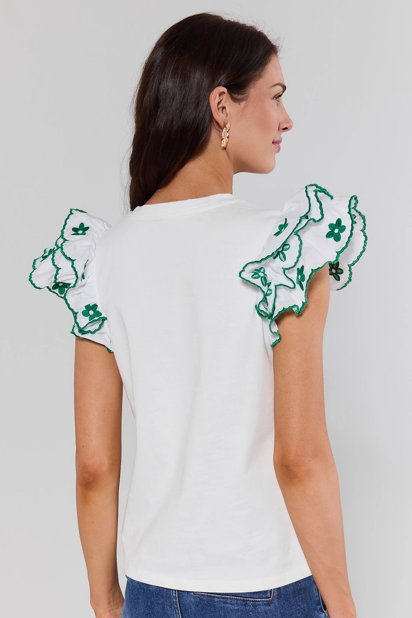 Woman standing wearing a white blouse with green floral embroidery on sleeves against a gray background