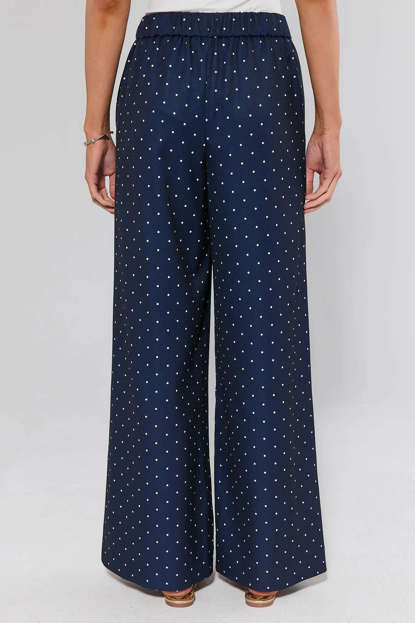 Navy blue wide-leg pants with white dot pattern worn by a person on a light gray background