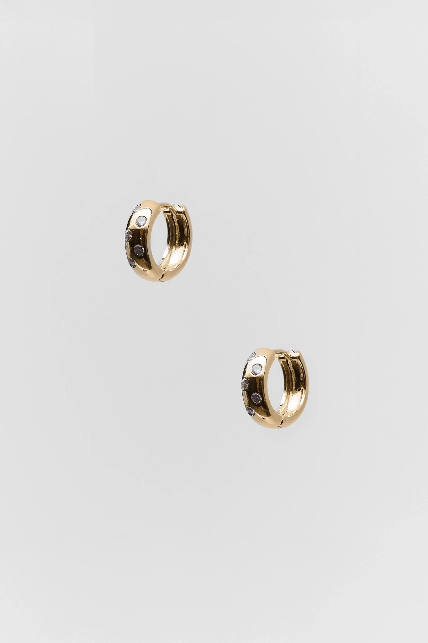 Gold hoop earrings with embedded stones on a light gray background