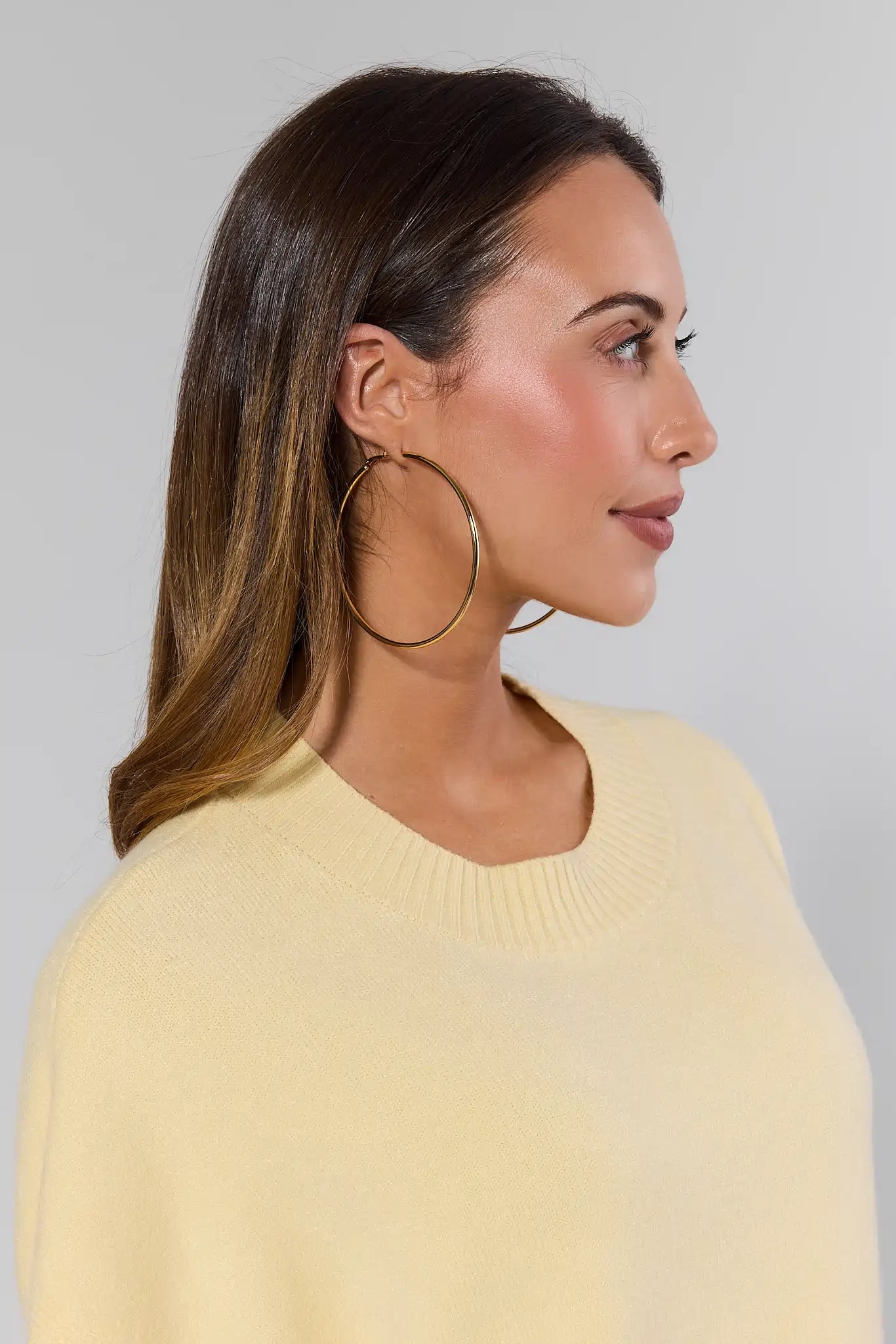 Woman wearing gold hoop earrings with a plain background