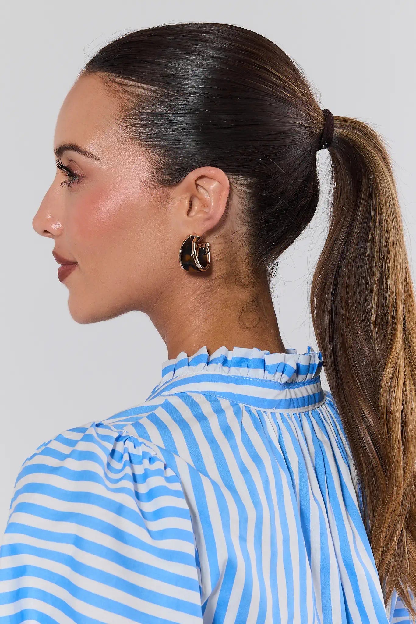 Woman wearing a blue and white striped shirt with a ponytail against a plain background