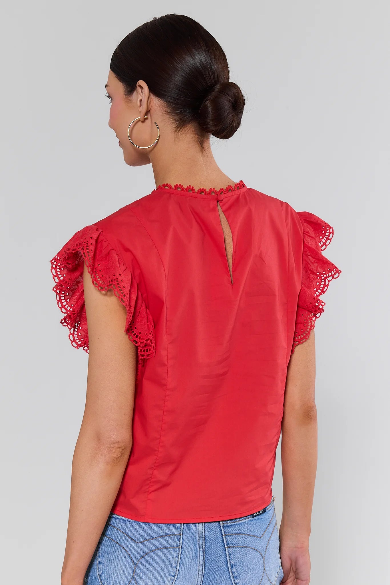 standing Woman wearing a red blouse with ruffled sleeves on a plain background