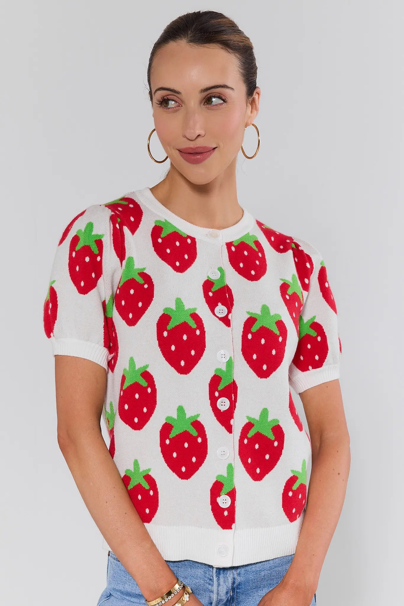 Woman wearing a white sweater with red strawberry pattern on a plain background