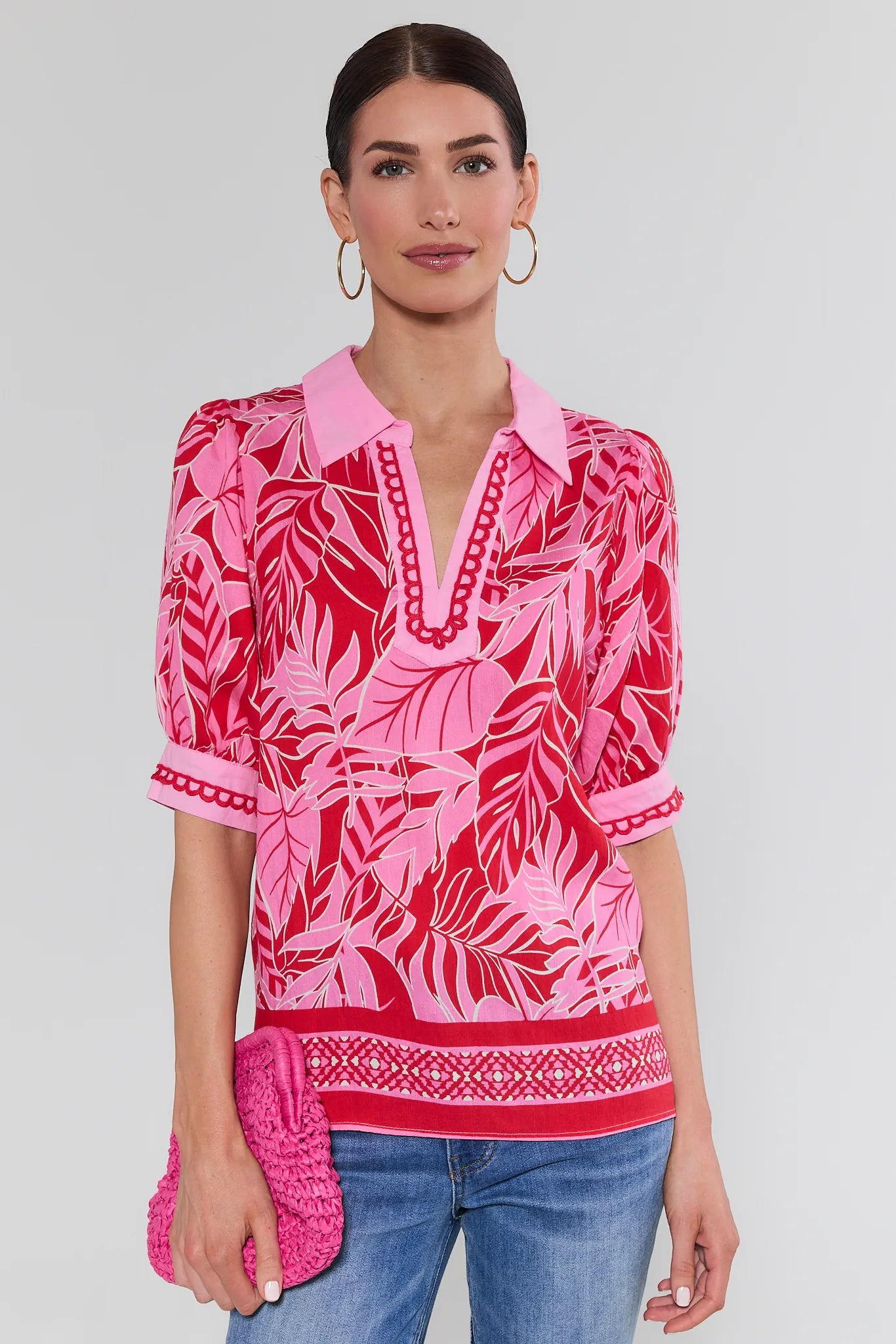 Woman wearing a pink and red patterned blouse with blue jeans on a white background