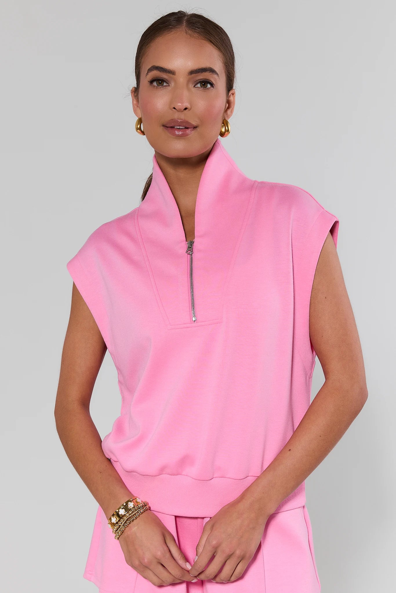 Woman wearing a pink sleeveless top with a zipper on a gray background
