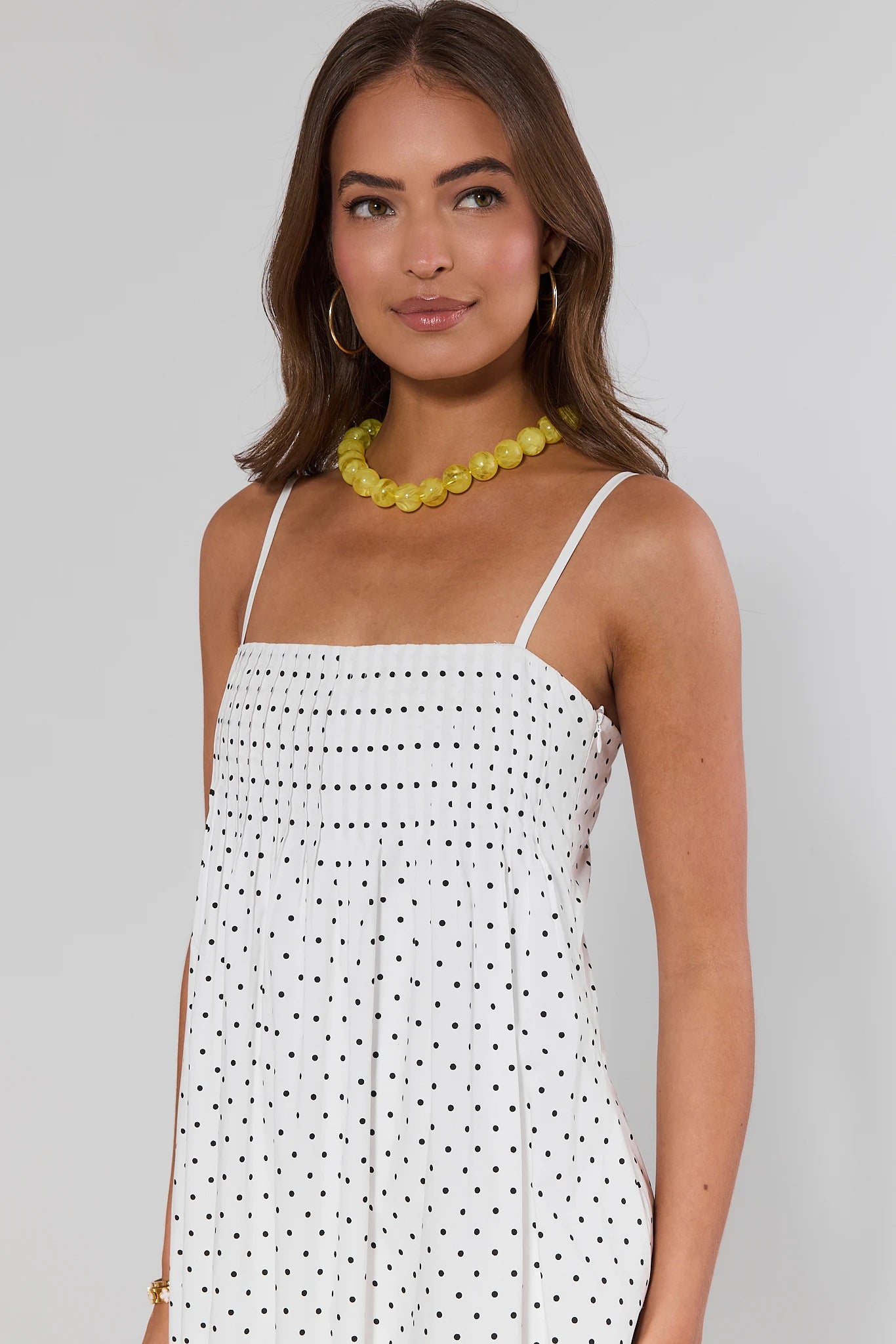 close up Woman wearing a white dress with black polka dots and a yellow necklace on a gray background