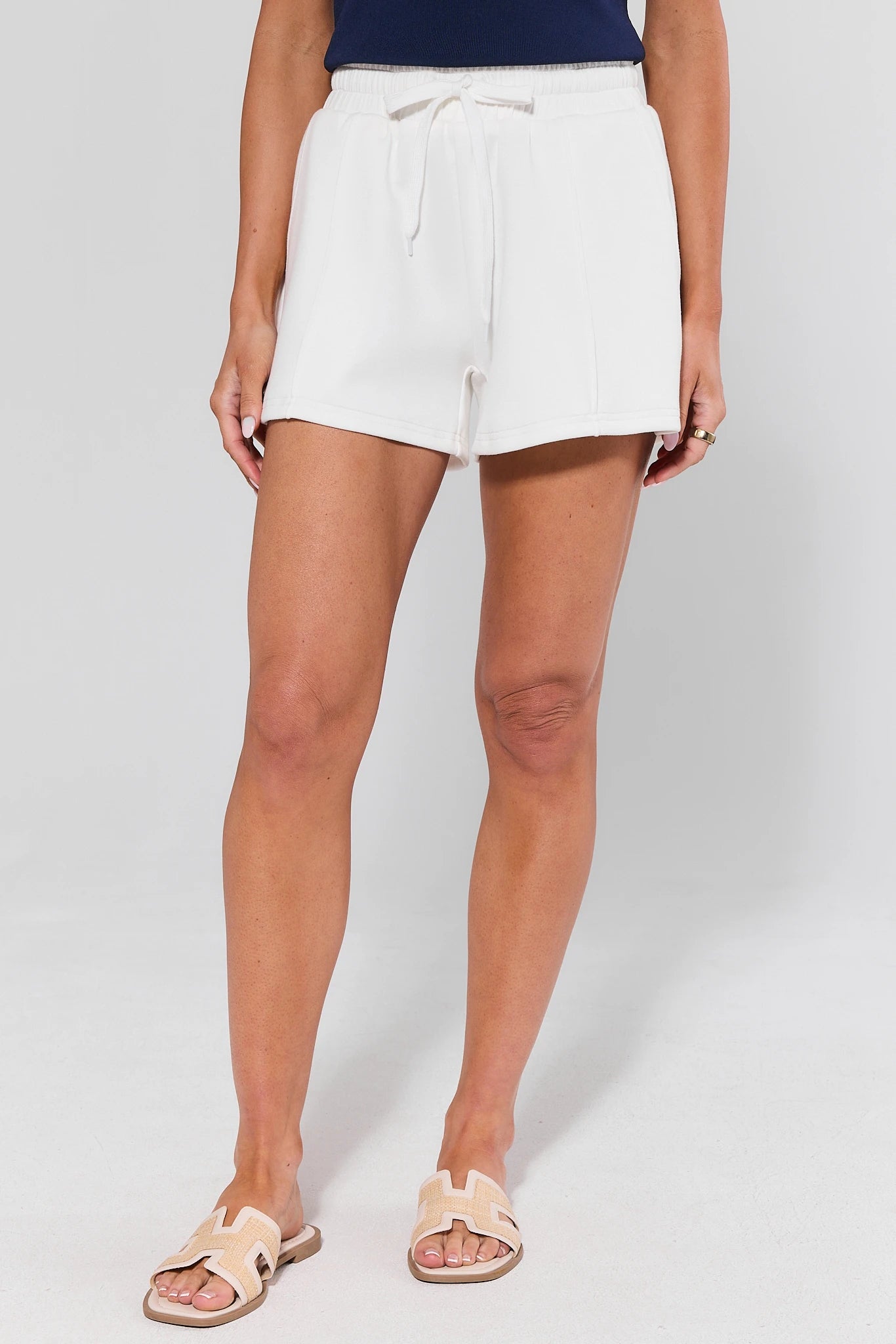 Person wearing white shorts and sandals on a plain background