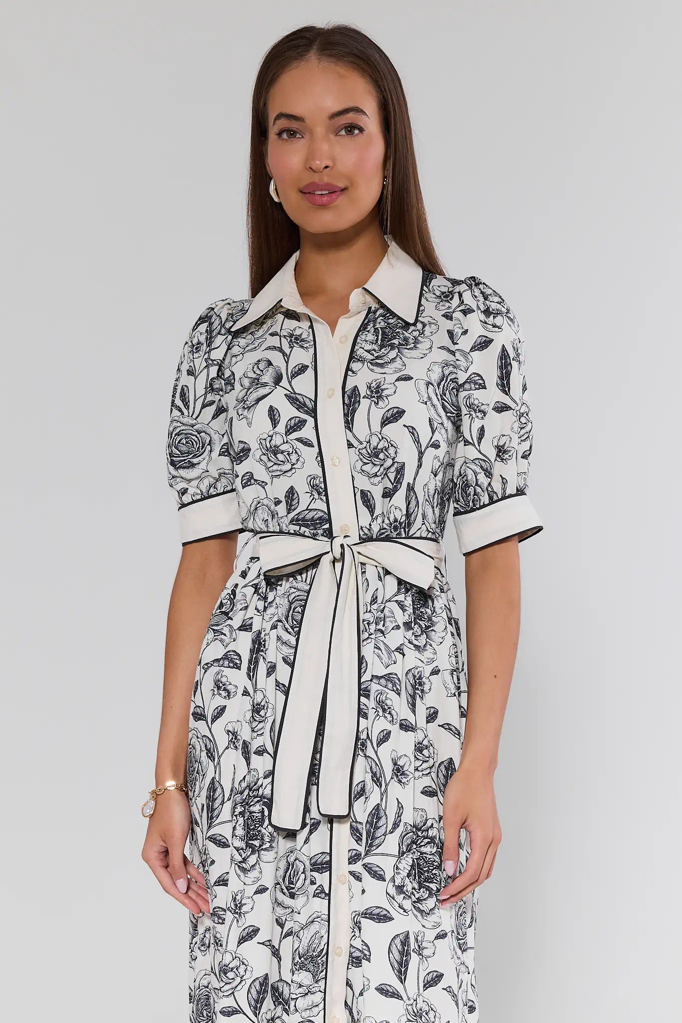 Woman wearing a black and white floral dress with a belt on a plain background