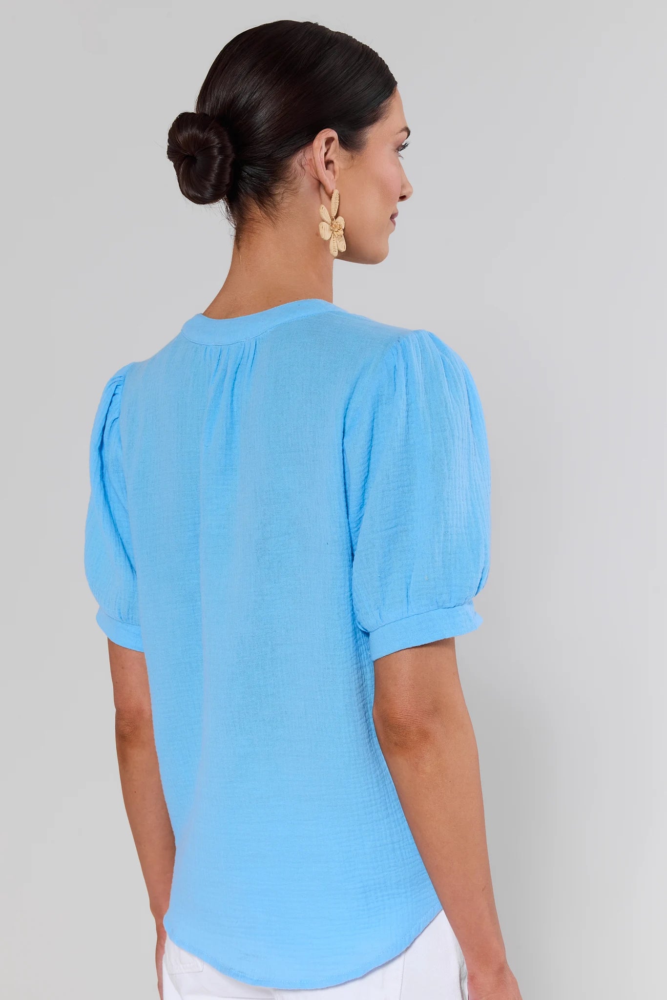 Woman standing wearing a light blue blouse with short sleeves on a gray background