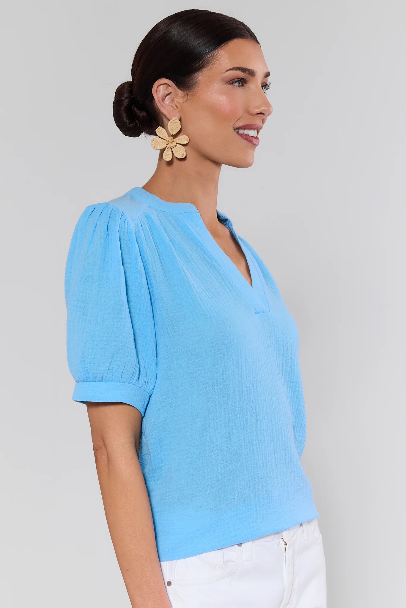 side shot Woman wearing a light blue blouse with white pants against a gray background