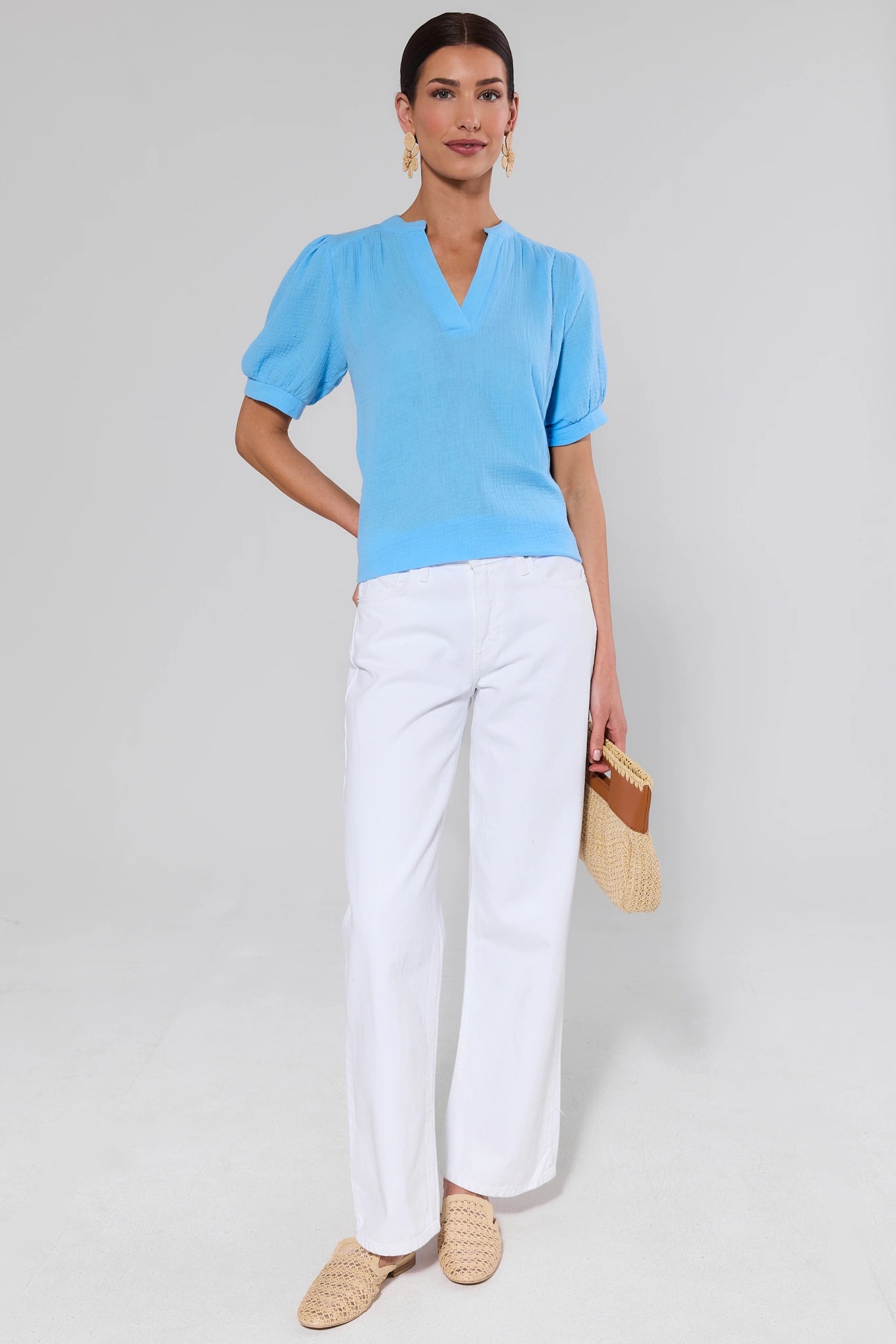 Woman wearing a light blue top and white pants against a background