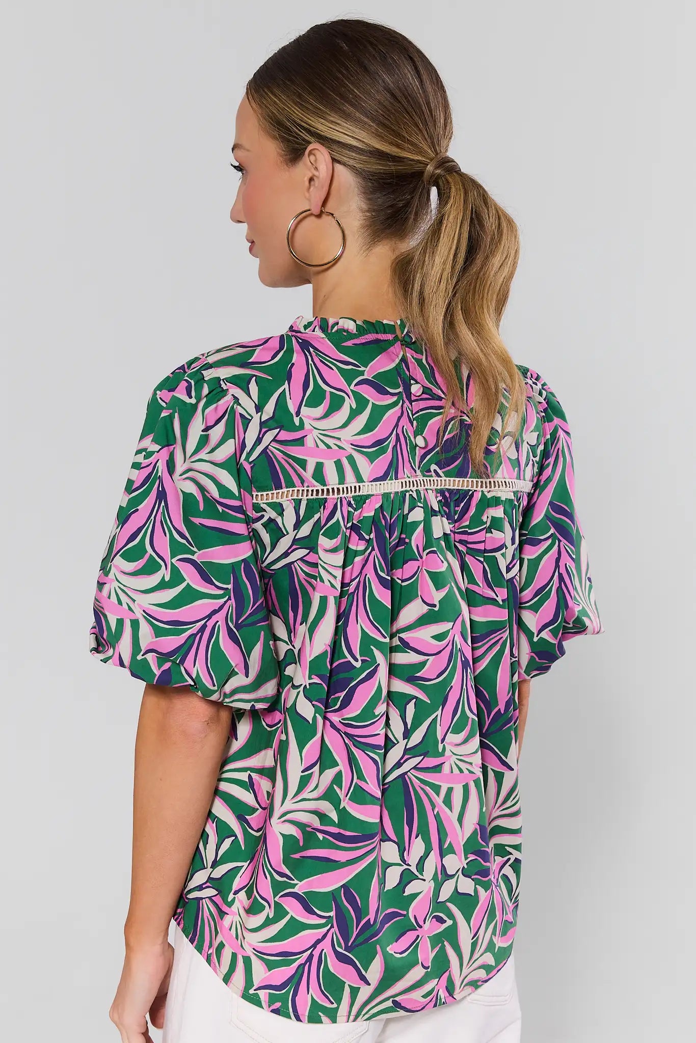 Woman standing wearing a colorful leaf-patterned blouse against a plain background