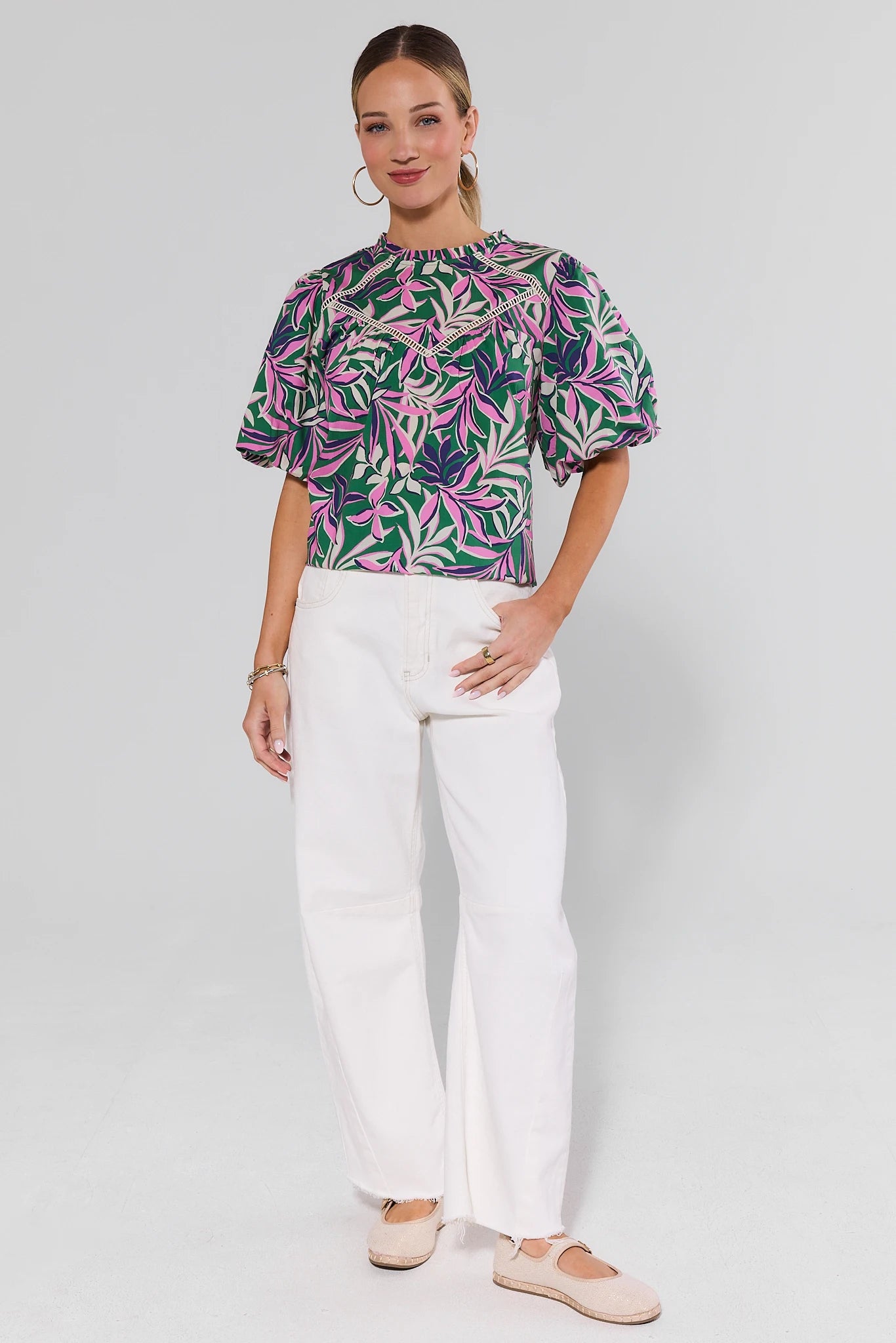 Woman wearing a colorful floral blouse and white pants on a plain background