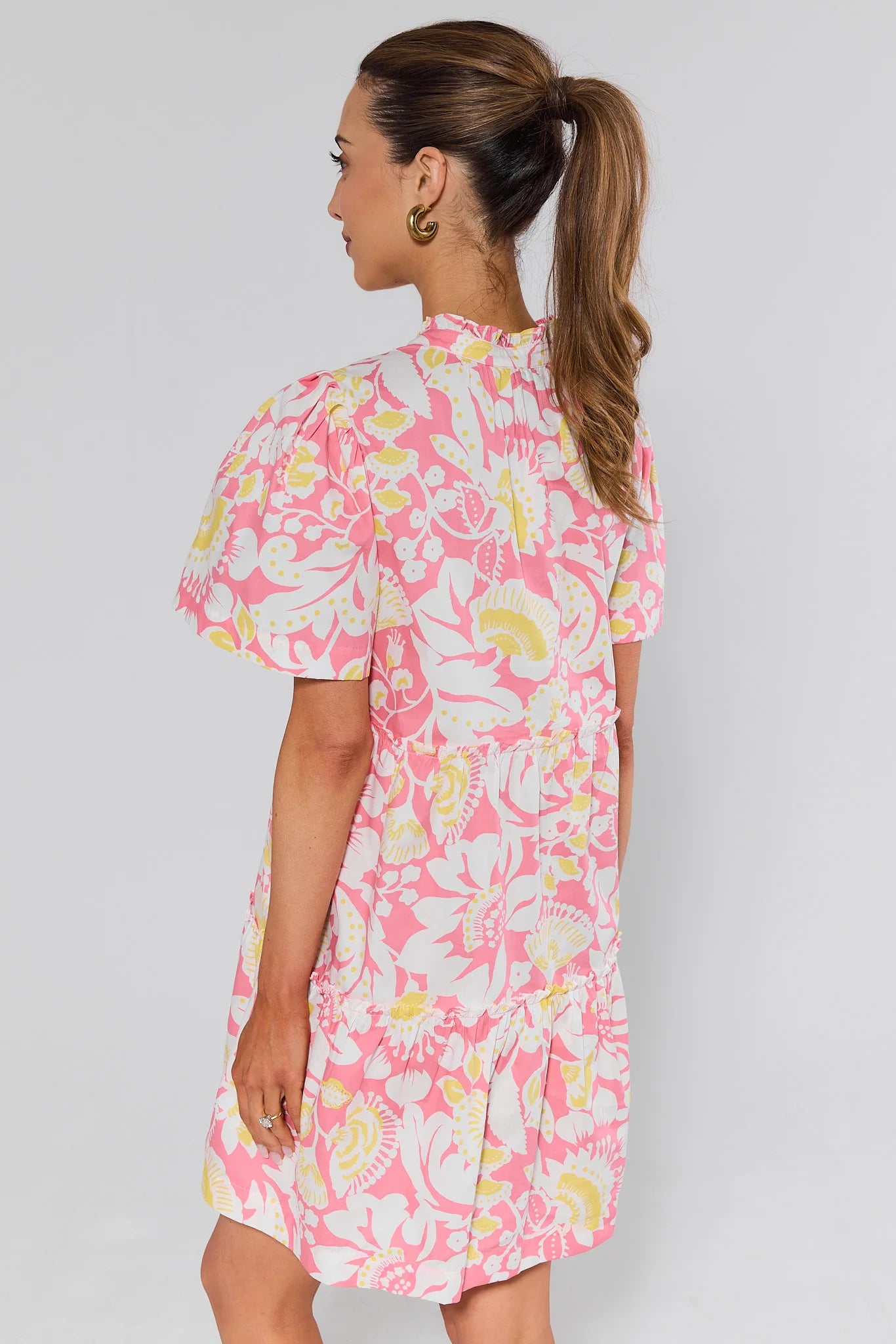 Woman standing wearing a pink floral dress against a plain background
